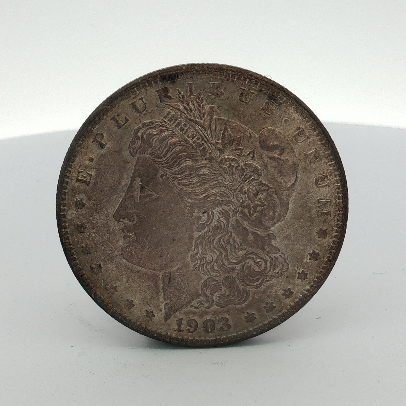 1903 US One Dollar Morgan Silver Dollar, Circulated: This US Morgan silver dollar was struck at the Philadelphia Mint in 1903. The coin is composed of 90% silver and 10% copper. It features the Morgan design with a Liberty head obverse and a heraldic ea