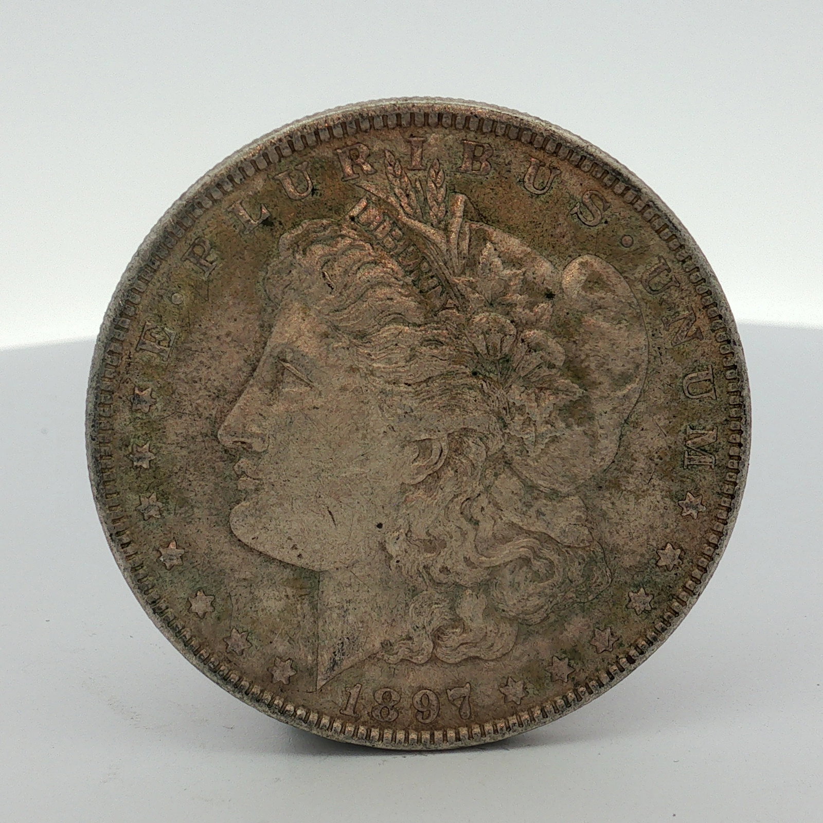 1897 US Morgan Silver Dollar Coin Circulated: This US 1897 Morgan silver dollar was struck at the Philadelphia Mint. The coin is composed of 90 percent silver and 10 percent copper. The obverse features the Liberty head design, while the reverse 