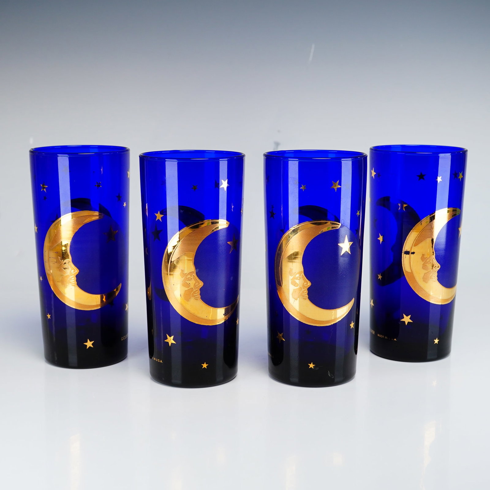 Set of Four Culver Cobalt Blue Celestial Moon and Stars Glass Tumblers: Four tall glass tumblers are manufactured by Culver Ltd. and features the Celestial pattern. Each vessel is constructed from deep cobalt blue glass and is decorated with a gold-tone Man in the Moon cr