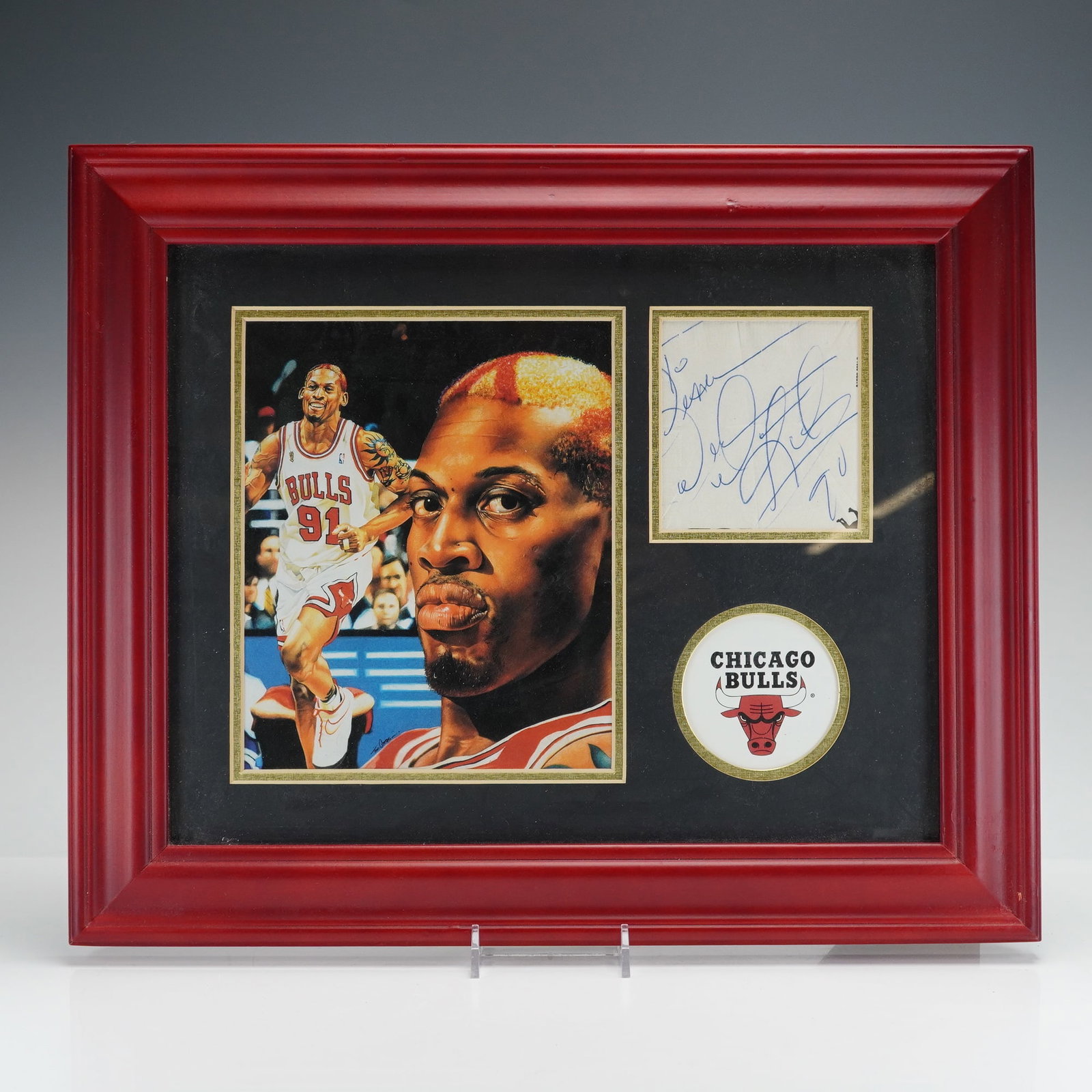 Dennis Rodman Signed Chicago Bulls Framed Memorabilia Display: This framed sports memorabilia display commemorates Dennis Rodman during his career with the Chicago Bulls. The display is housed in a red-finished wooden frame with a black mat featuring three distin