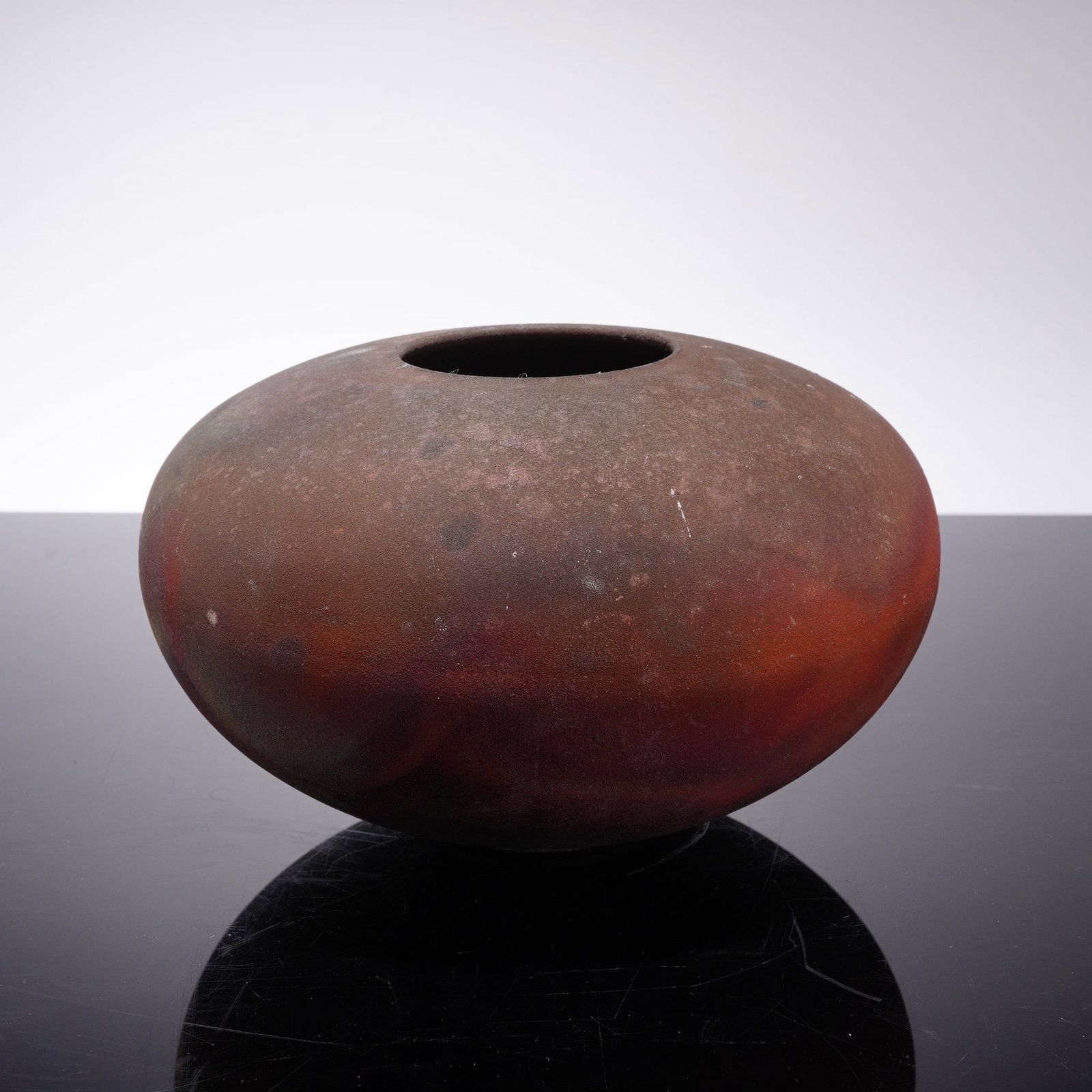 Contemporary Raku Fired Iridescent Studio Art Pottery Bowl, Signed: This handmade studio art pottery bowl is designed in a compressed globular seed form featuring a small circular mouth and a rounded base. The vessel is finished with a variegated iridescent glaze achi
