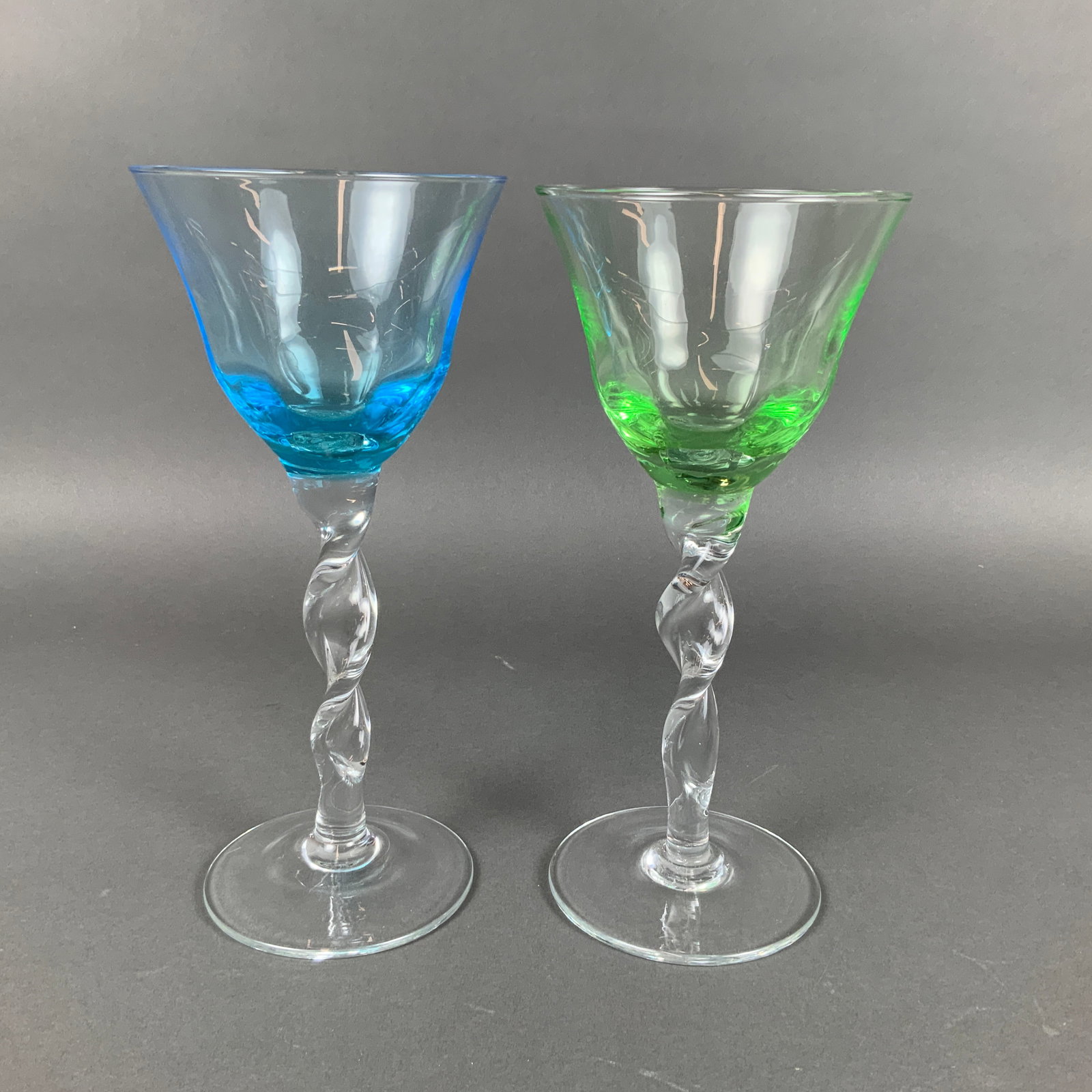 2pc Abigails Adriana Pattern Wine Glasses: This pair of blown glass stems is attributed to Abigails in the Adriana pattern. The lot consists of two glasses featuring flared bowls in azure blue and lime green. Each bowl is supported by a clear,