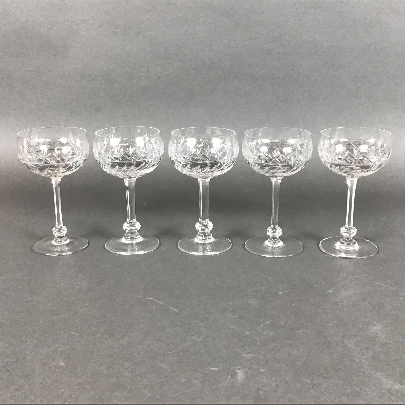5pc Cut Crystal Cordial Glasses: This set of five cut crystal cordial or liqueur glasses features a wide, shallow bowl construction. The decoration consists of a horizontal band of cut starburst and pinwheel motifs situated above a s