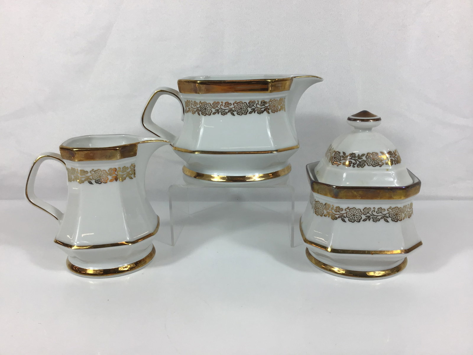 3pc Winterling Marktleuthen Bavaria Porcelain Tea Service Pieces: This trio of white porcelain service items is produced by Winterling in Marktleuthen, Bavaria. The set includes a creamer, a small pitcher, and a lidded sugar bowl. Each piece features an octagonal fa