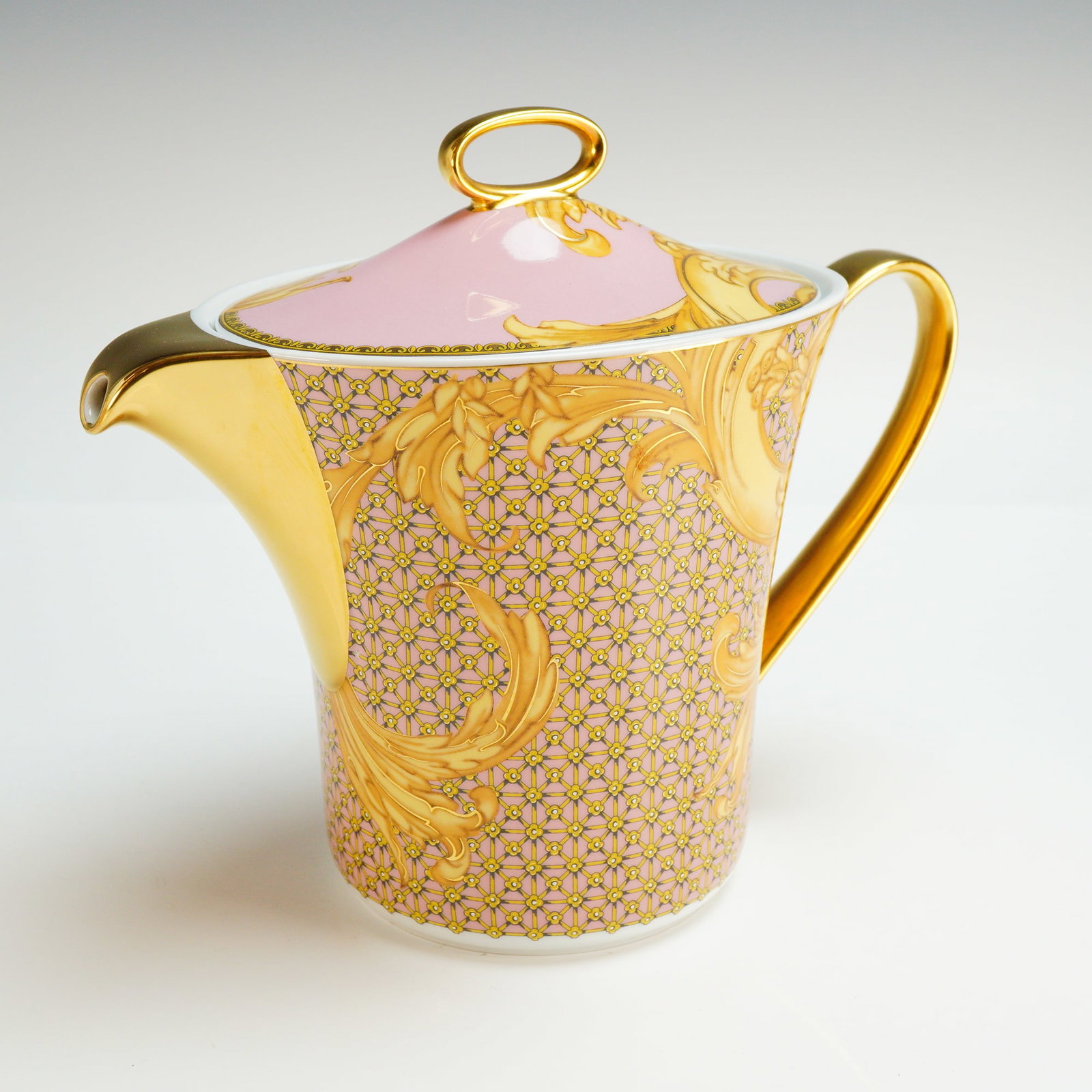Versace Rosenthal Porcelain Lidded Teapot, Les Reves Byzantins: The vessel features a pink ground decorated with a golden floral trellis pattern and acanthus leaf scrolls. The piece is constructed with a gilded spout and a curved gilded handle. The matching lid is