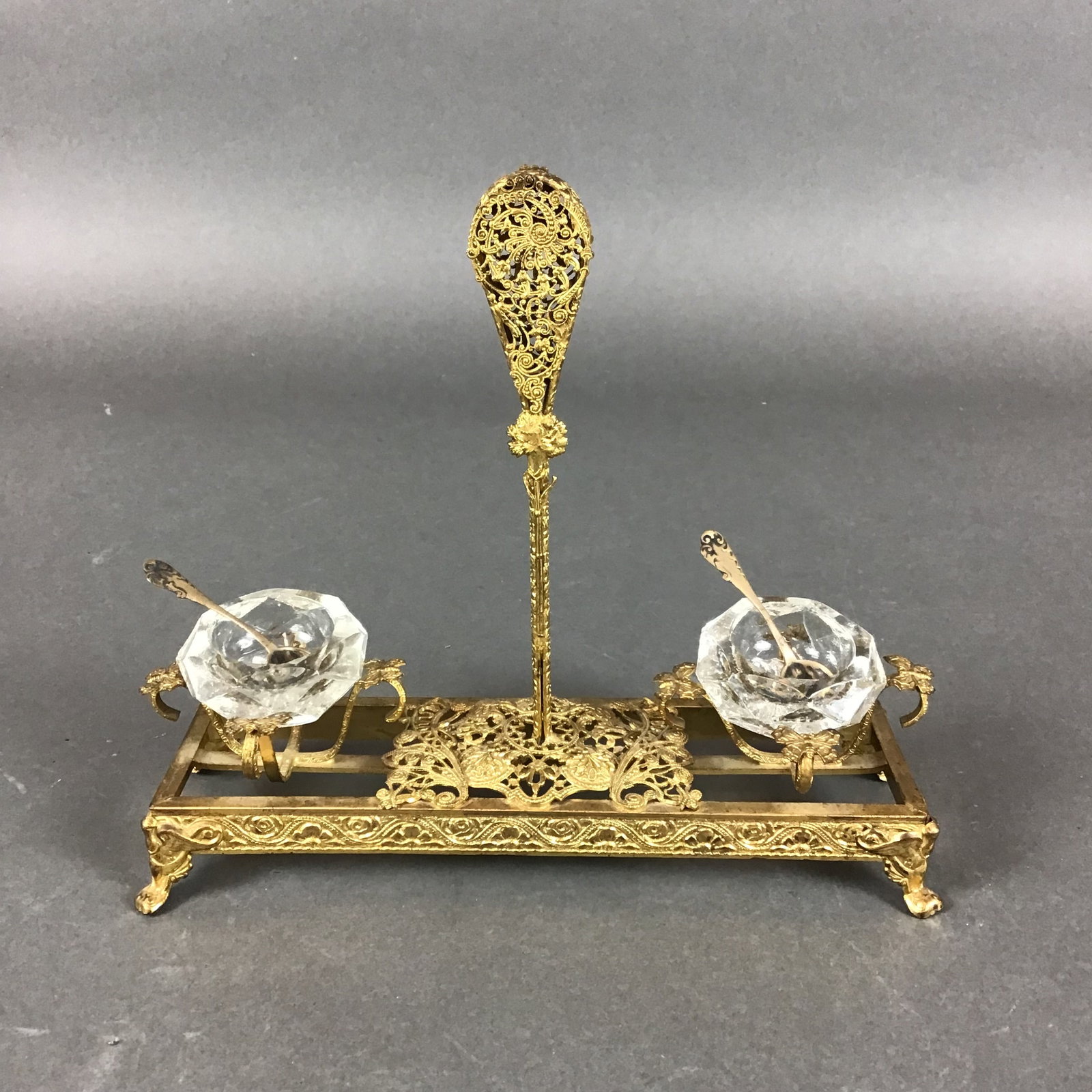 Gilt Metal Double Open Salt Cellar Stand with Glass Liners and Sterling Silver Spoons: This gilt metal double open salt cellar stand features a rectangular openwork frame supported by four scroll-and-leaf feet. The metal holder is decorated with cast scrollwork and foliate patterns thro