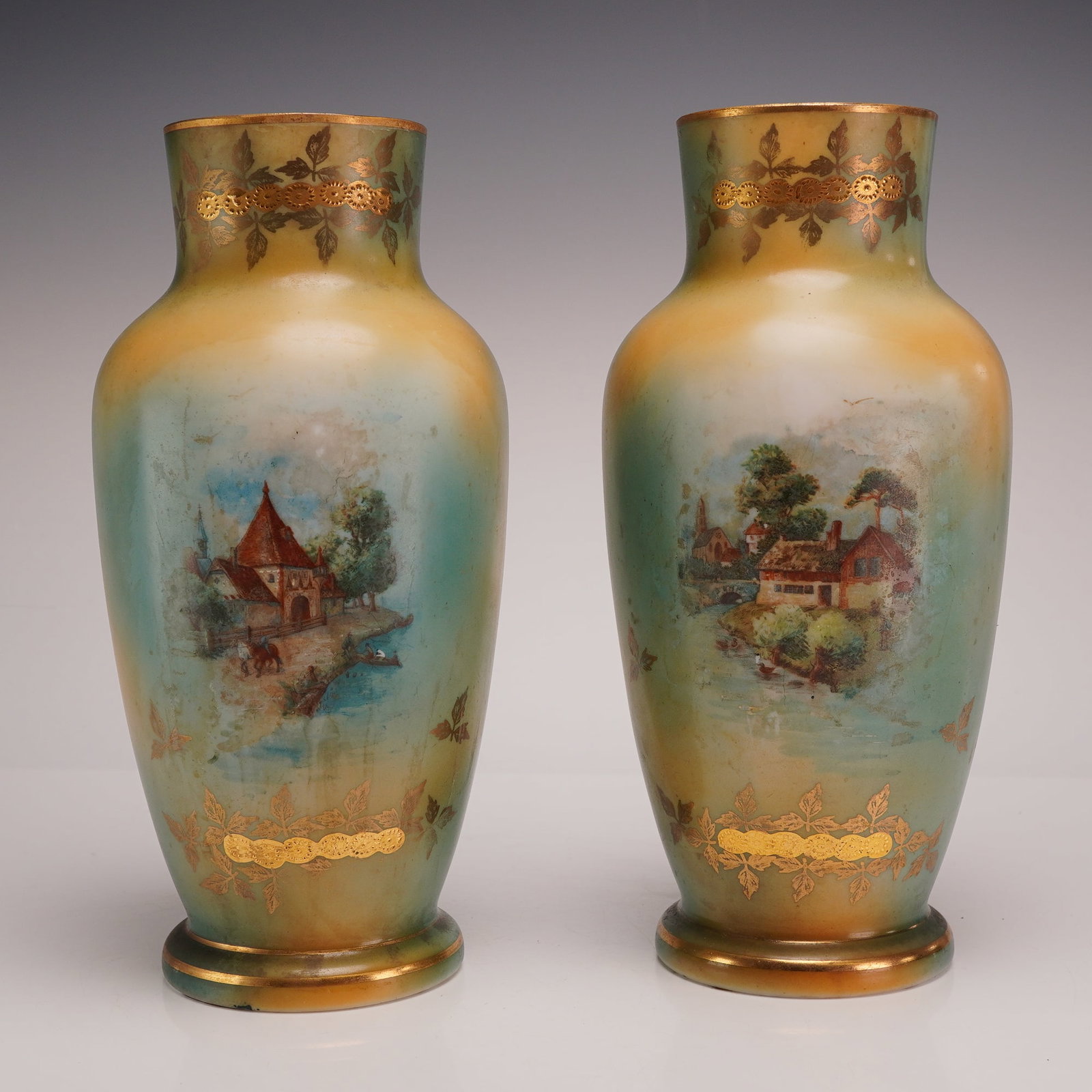 Pair of Enameled Art Glass Pastoral Landscape Vases: The glass exhibits a mottled, blended background of soft greens, yellows, and blues. Each vase is decorated with a unique hand-painted enamel pastoral landscape. One scene depicts a building with a st