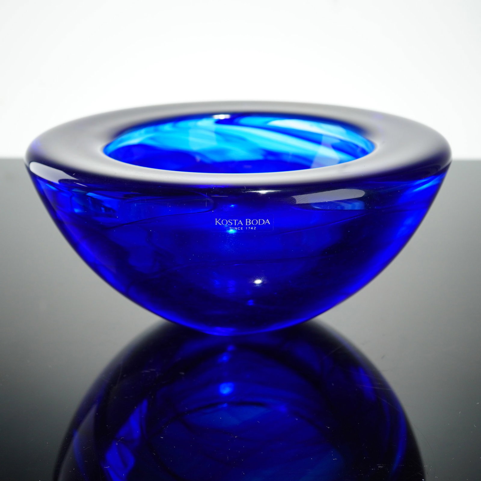 Anna Ehrner for Kosta Boda Cobalt Blue Art Glass Bowl, Atoll: This hand-blown art glass bowl is from the Atoll series designed by Anna Ehrner for Kosta Boda, Sweden. The piece is constructed of heavy, thick-walled cobalt blue glass featuring internal organic swi