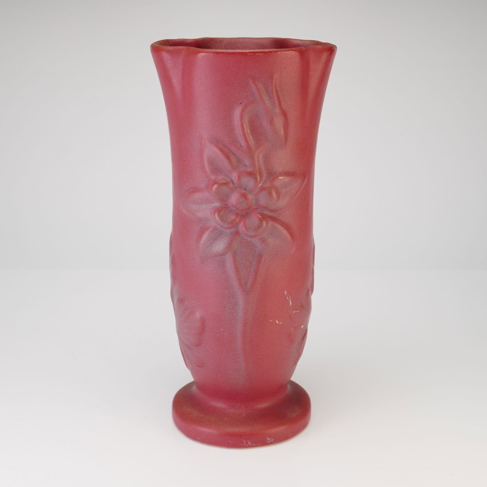 Van Briggle Pottery Columbine Vase, Persian Rose: Earthenware vase slightly waisted cylindrical form, rising to a scalloped rim and set on a circular pedestal foot. The exterior is finished in a uniform matte Persian Rose glaze. Decorated with molded