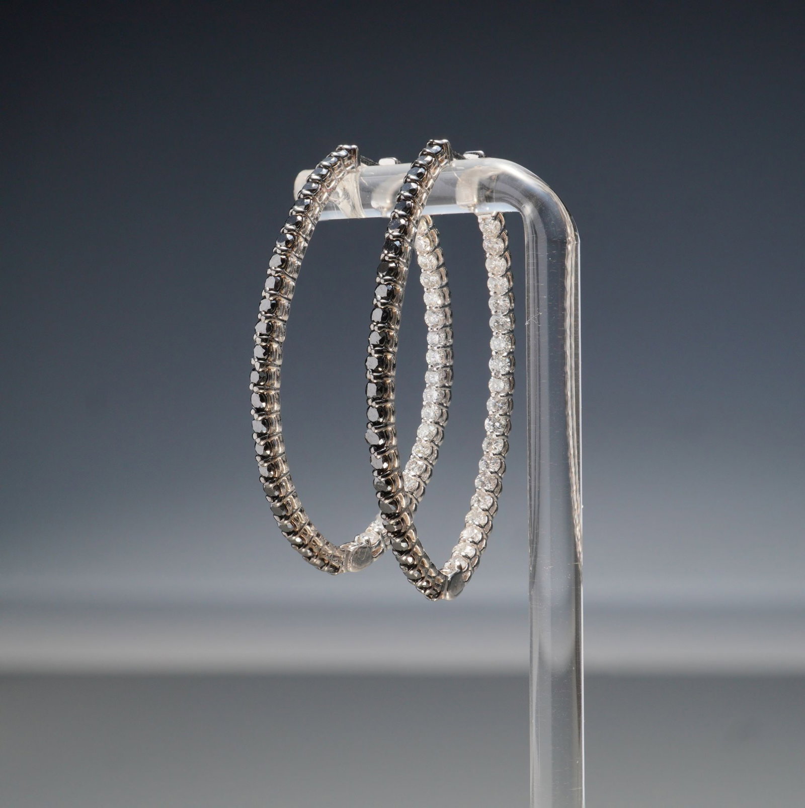 Pair of 14K White Gold 2.77ctw Black & White Diamond Oval Hoop Earrings: A striking pair of 14K white gold oval hoop earrings set with a total of 2.77 carats of round black and white diamonds. The distinctive design features contrasting stones, with black diamonds adorning