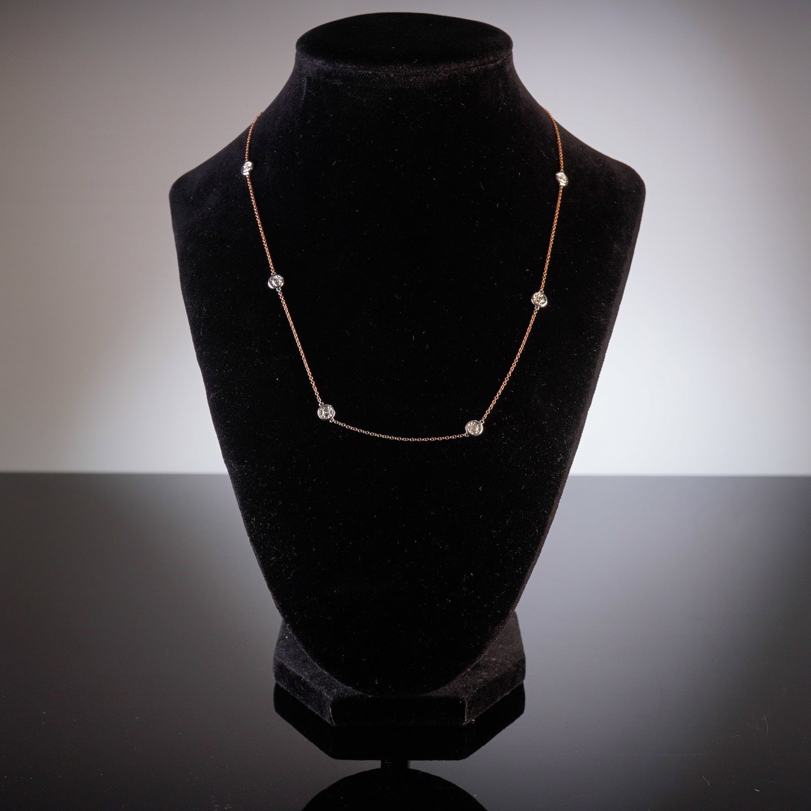 14K Rose and White Gold 0.16ctw Diamond Station Necklace: The necklace features a fine link rose gold chain interspersed with eight round bezel-set diamonds. Each diamond is mounted within a white gold circular setting. The piece is secured by a lobster claw