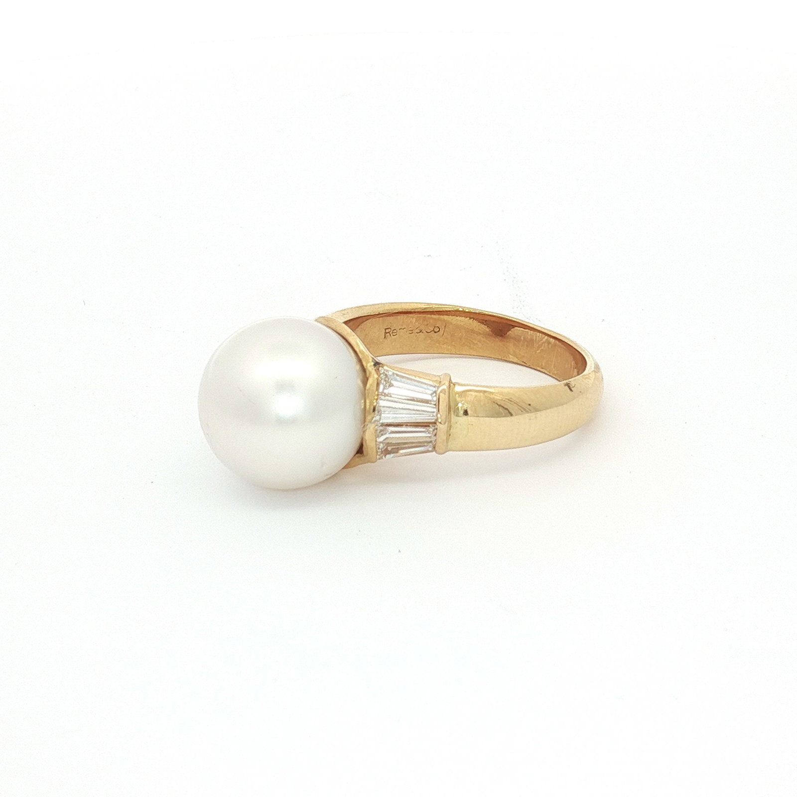 18K Yellow Gold Ring with Round White Pearl and Baguette Diamonds: An estate ring crafted in 18K yellow gold. The ring features a large, round white pearl center stone secured in a raised mounting. Flanking the center stone on each shoulder are several channel-set, b