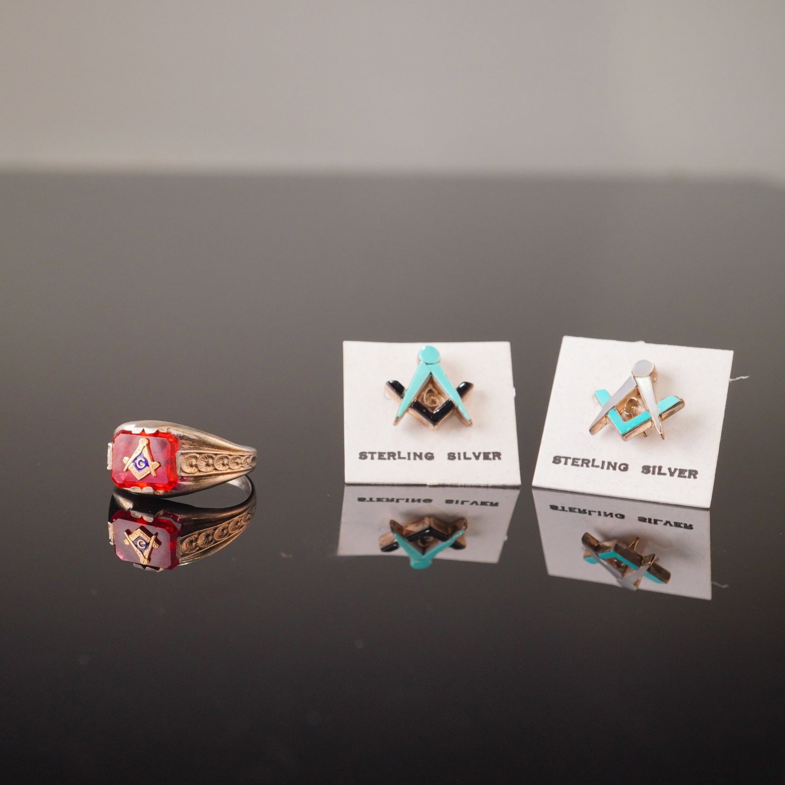 Trio of Masonic Fraternal Jewelry Pieces Including One Ring and Two Pins: This lot consists of three pieces of Masonic fraternal jewelry including one signet-style ring and two lapel pins. The signet ring is crafted from sterling silver and is stamped STERLING on the interi