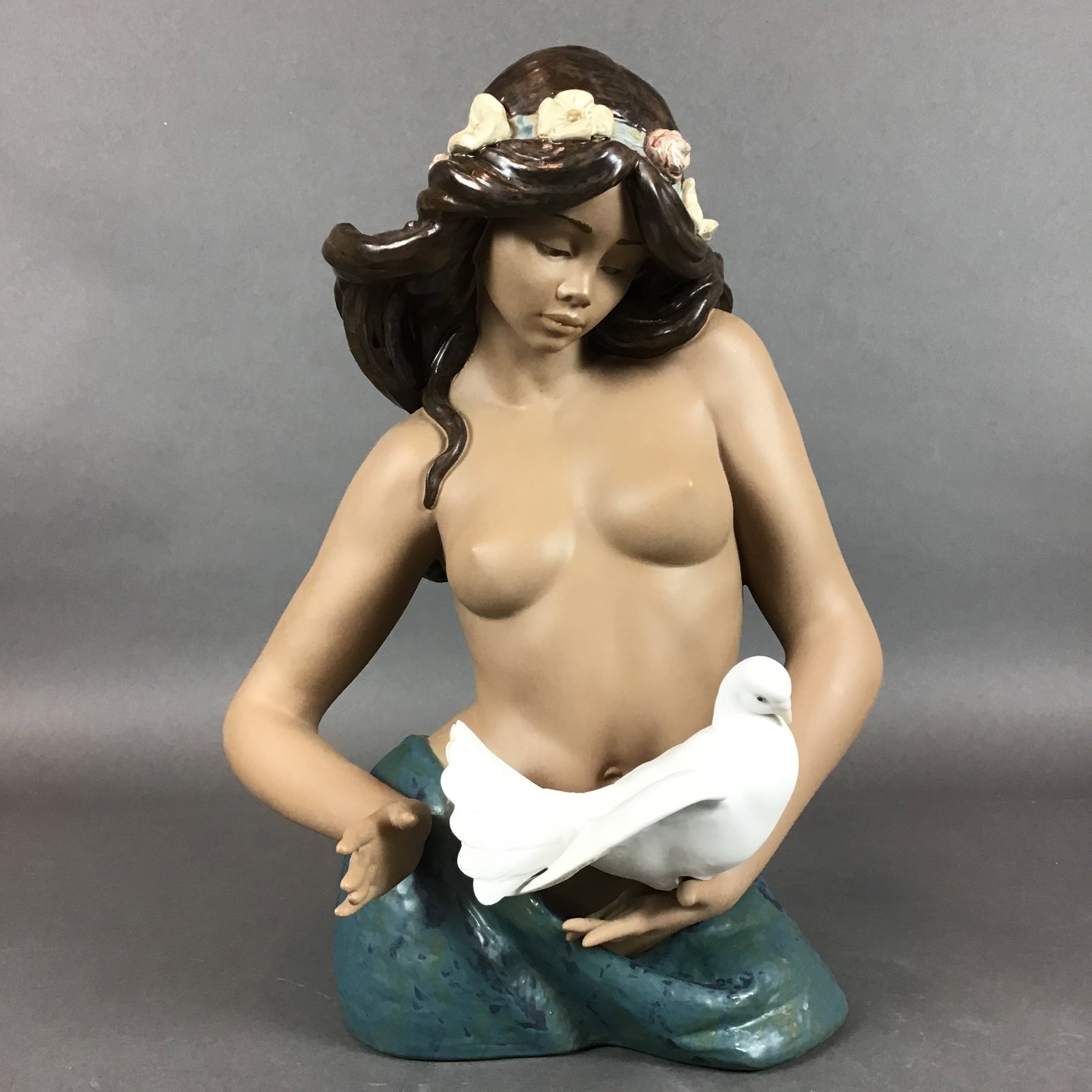 Lladro Porcelain Sculpture, A Tribute to Peace, Model 2150: A Lladro porcelain bust depicting a partially nude woman holding a white dove. The figure is rendered with a combination of finishes, featuring matte bisque skin and a high-gloss glaze on the hair, th