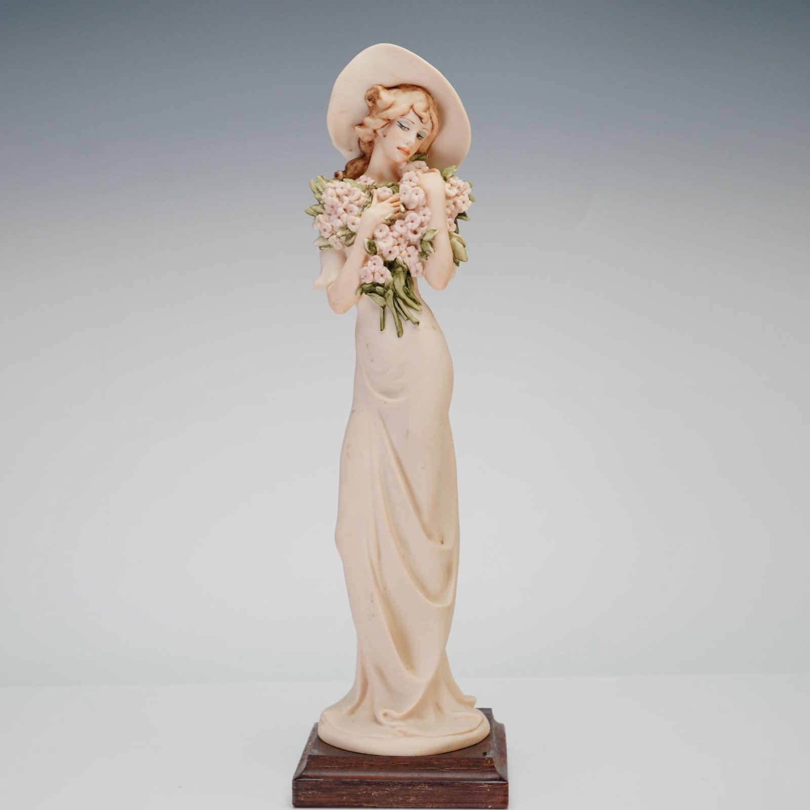 Giuseppe Armani Florence Figurine Lilac 1995F: This cold-cast porcelain figurine, titled Lilac, was produced by Florence Sculture d'Arte and designed by artist Giuseppe Armani. The figure depicts a woman in a floor-length cream gown and a wide-bri
