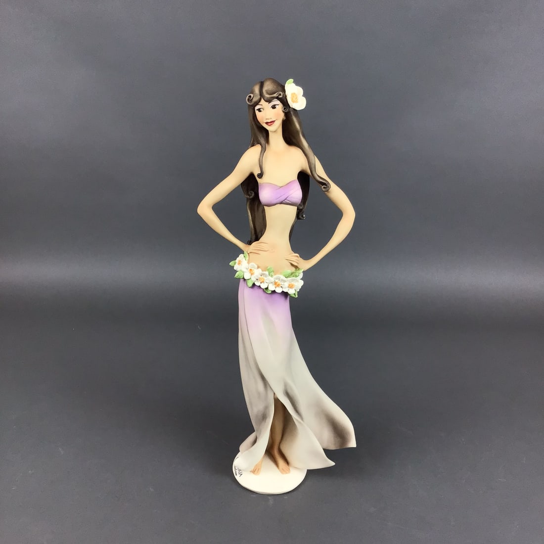 Giuseppe Armani Florence Studio Porcelain Figurine Maui Girl Model 2098P: A hand-painted matte-finish porcelain figurine produced by Giuseppe Armani for Florence Studio, titled Maui Girl. The figure is depicted in a confident pose with hands on hips, wearing a purple bandea