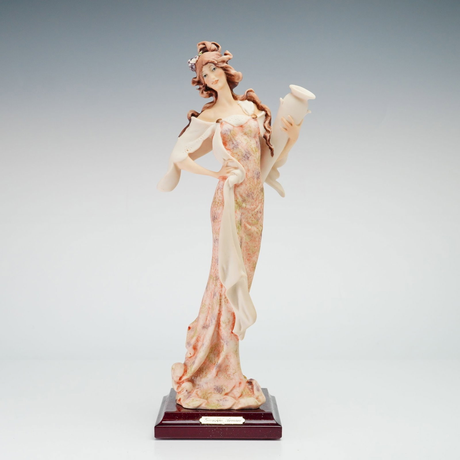 Giuseppe Armani for Florence Sculture d'Arte Figurine Girl with Pitcher 0959C: The figure is depicted holding a tall, slender pitcher and features flowing hair accented with small flowers. The long dress is decorated with a soft-toned floral pattern in pink, yellow, and green. T