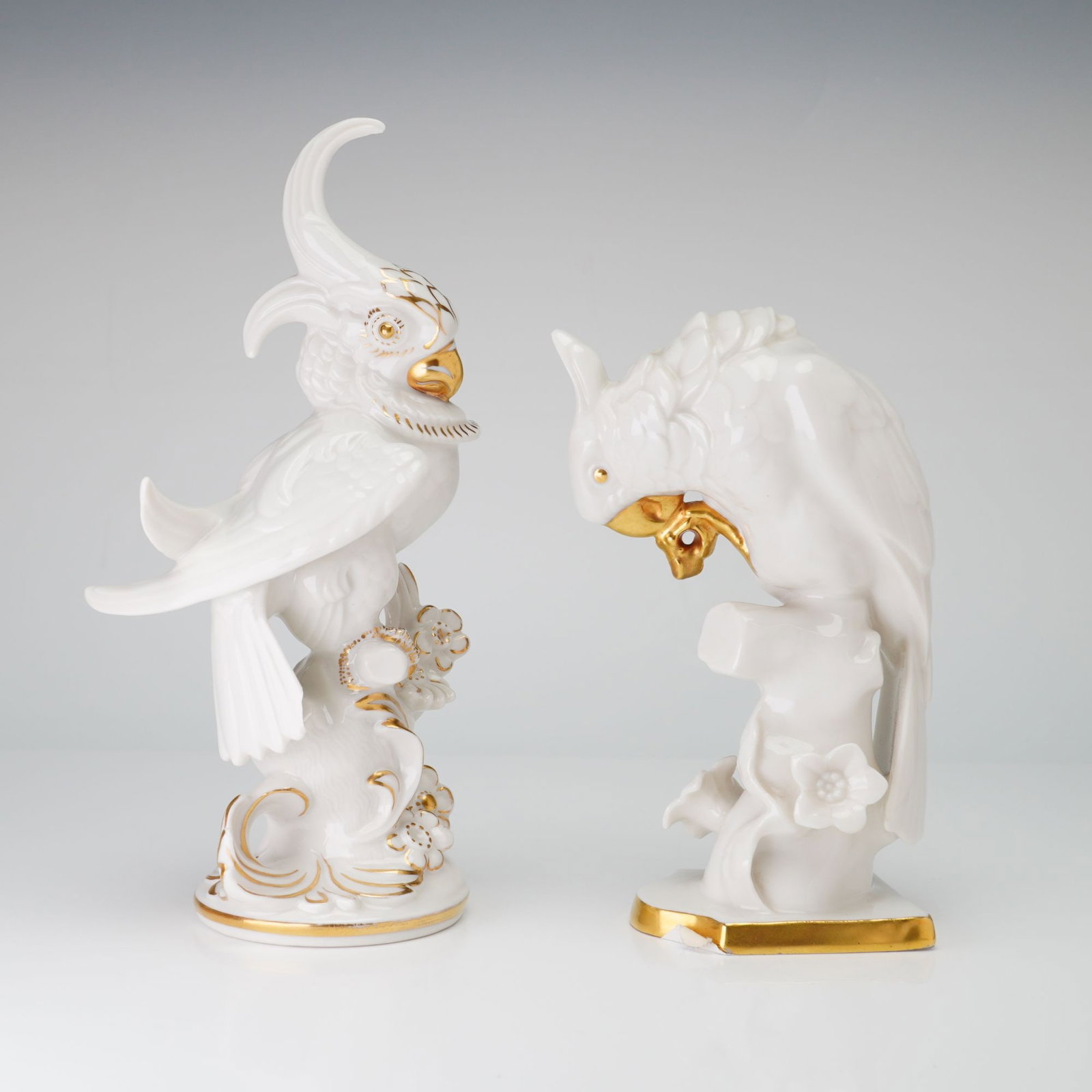 Two Hutschenreuther White Glazed Porcelain Cockatoo Figurines: The pieces are finished with overglaze gold highlights on the beaks, eyes, crests, and base rims. One bird is modeled in an upright stance with a raised crest, while the second bird is in a downward-l