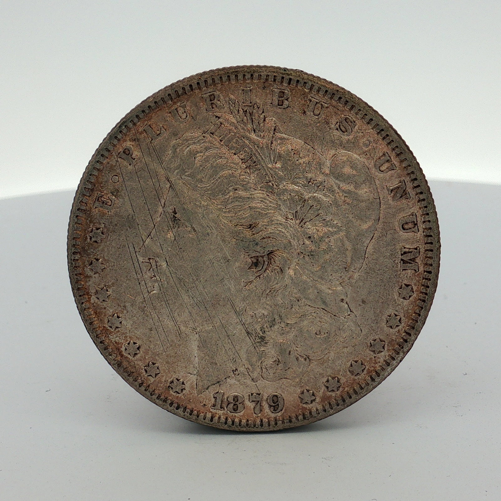 1879-O US Morgan Silver Dollar Coin Circulated: This US Morgan silver dollar was struck at the New Orleans Mint, as indicated by the O mint mark located on the reverse above the denomination. The coin is composed of silver and features a reeded edg