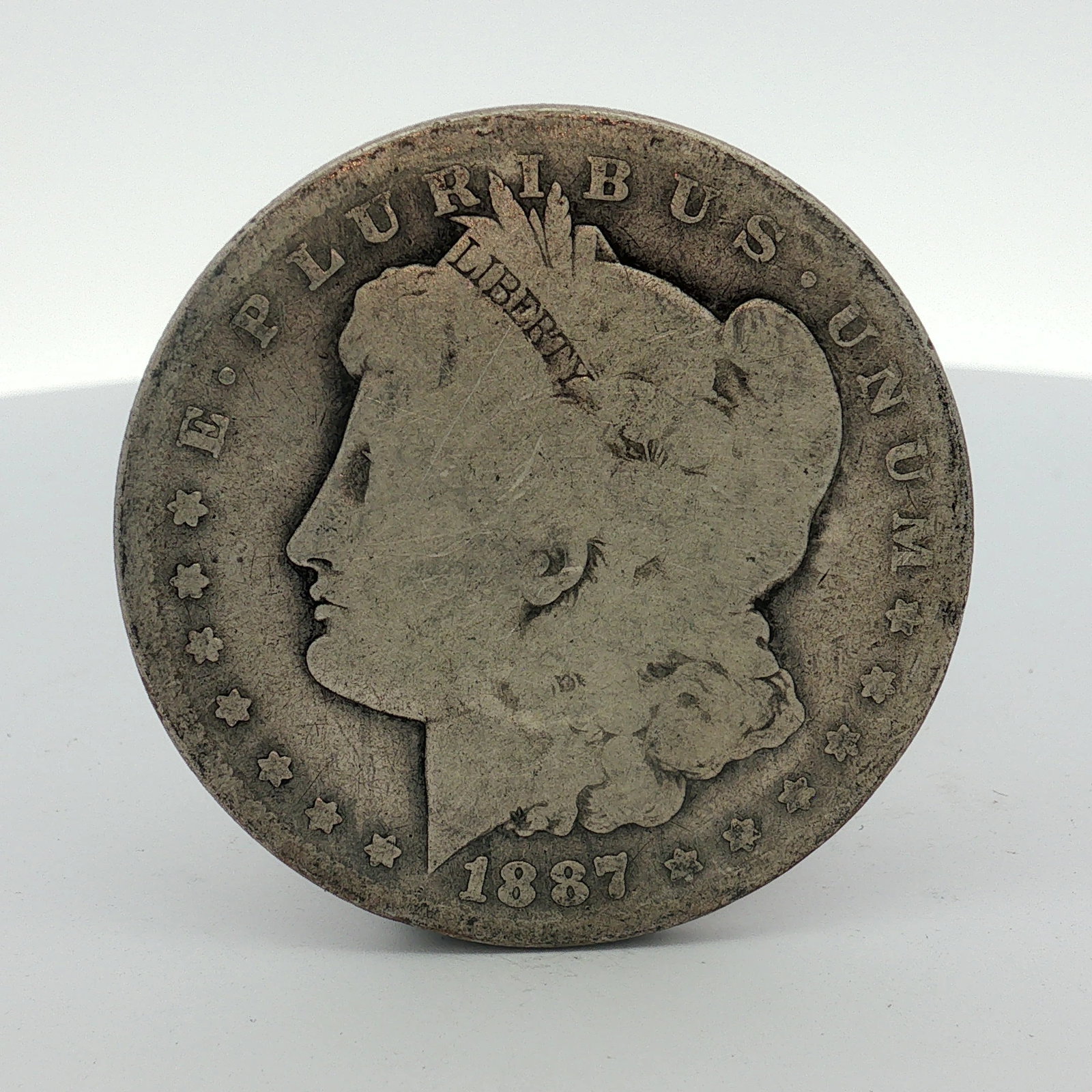 1887-O US Morgan Silver Dollar Coin Circulated: This US Morgan silver dollar is dated 1887 and was struck at the New Orleans Mint. The coin features the Liberty Head obverse and the Heraldic Eagle reverse. A raised O mint mark is visible on the rev