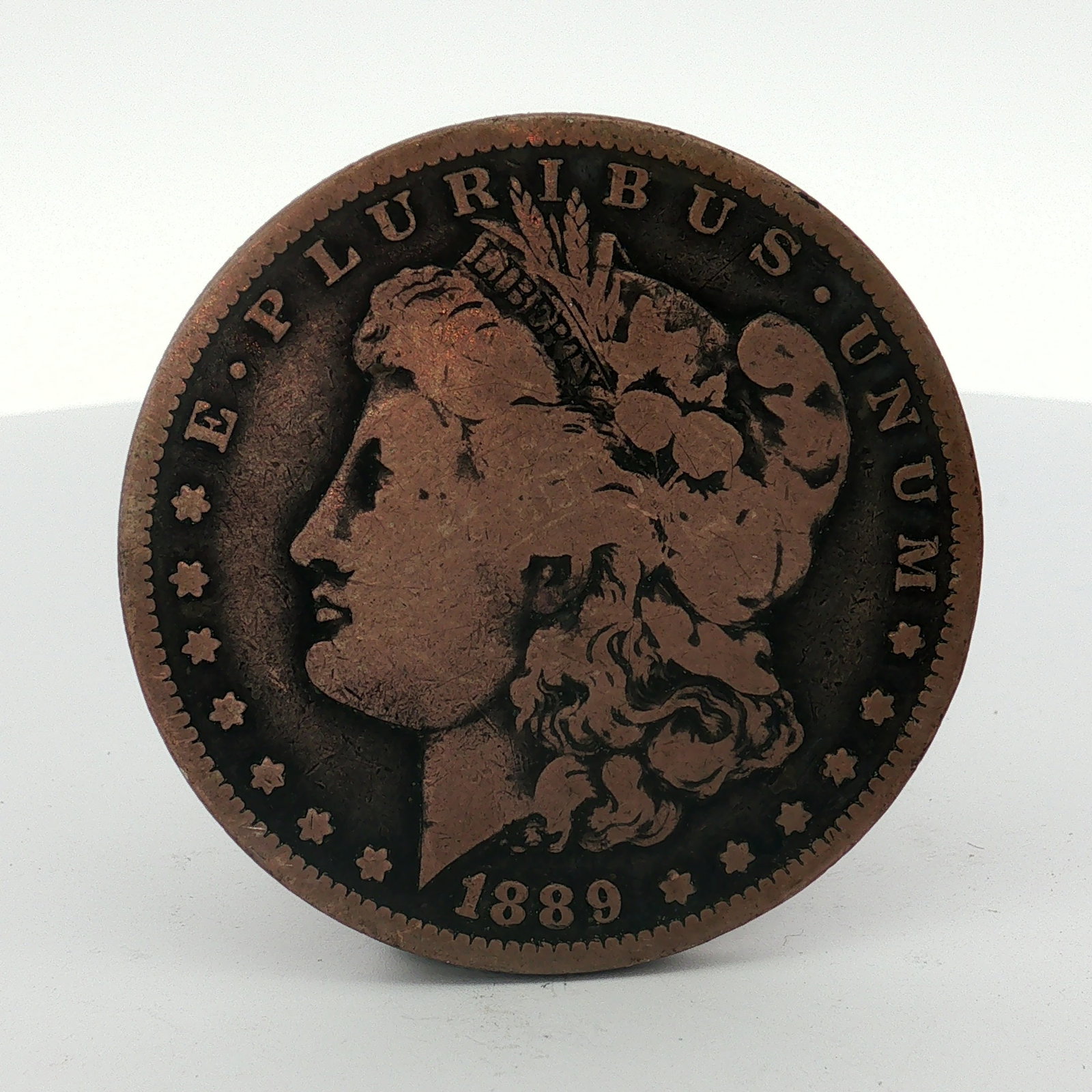 1889-O US Morgan Silver Dollar Coin Circulated: This item features the Morgan dollar design and is dated 1889 with an O mint mark for the New Orleans Mint. The piece is composed of a non-precious metal, exhibiting a deep brown, copper-like patina a