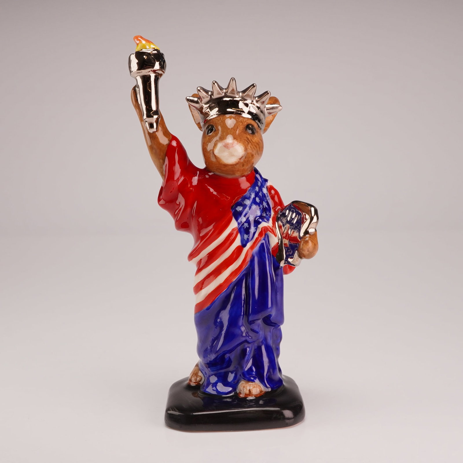 Royal Doulton Bunnykins Prototype Special Colorway Figurine, Statue of Liberty: Depicting a bunny in the guise of the Statue of Liberty. The ceramic figure is decorated in a patriotic palette featuring a red robe, a blue sash adorned with white stars, and a red and white striped 