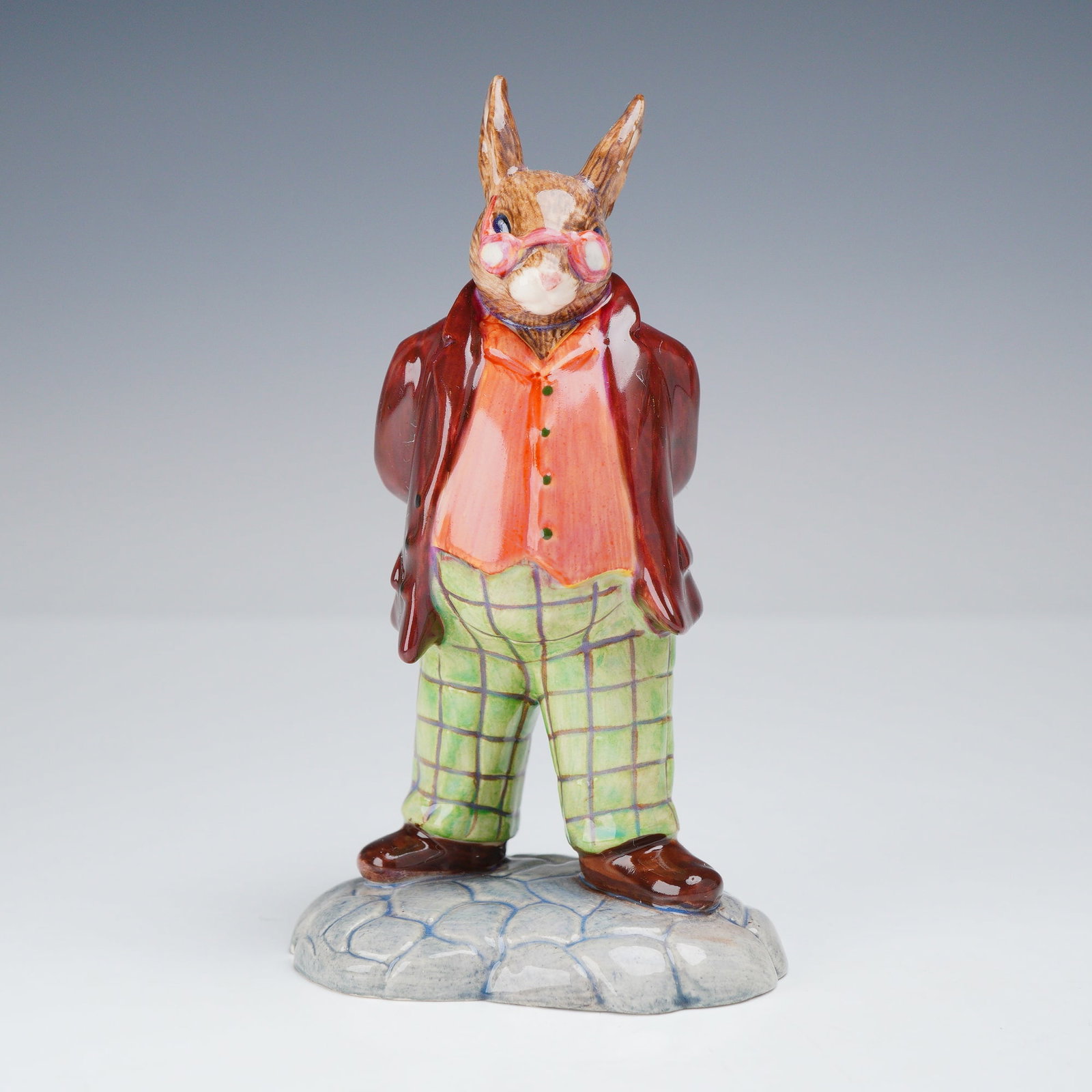 Royal Doulton Rare Prototype Father Bunnykins Figurine: This is a glazed ceramic figurine of Father Bunnykins produced by Royal Doulton. The anthropomorphic rabbit is depicted standing on a base with a cobbled-stone effect. He is wearing a dark red overcoa