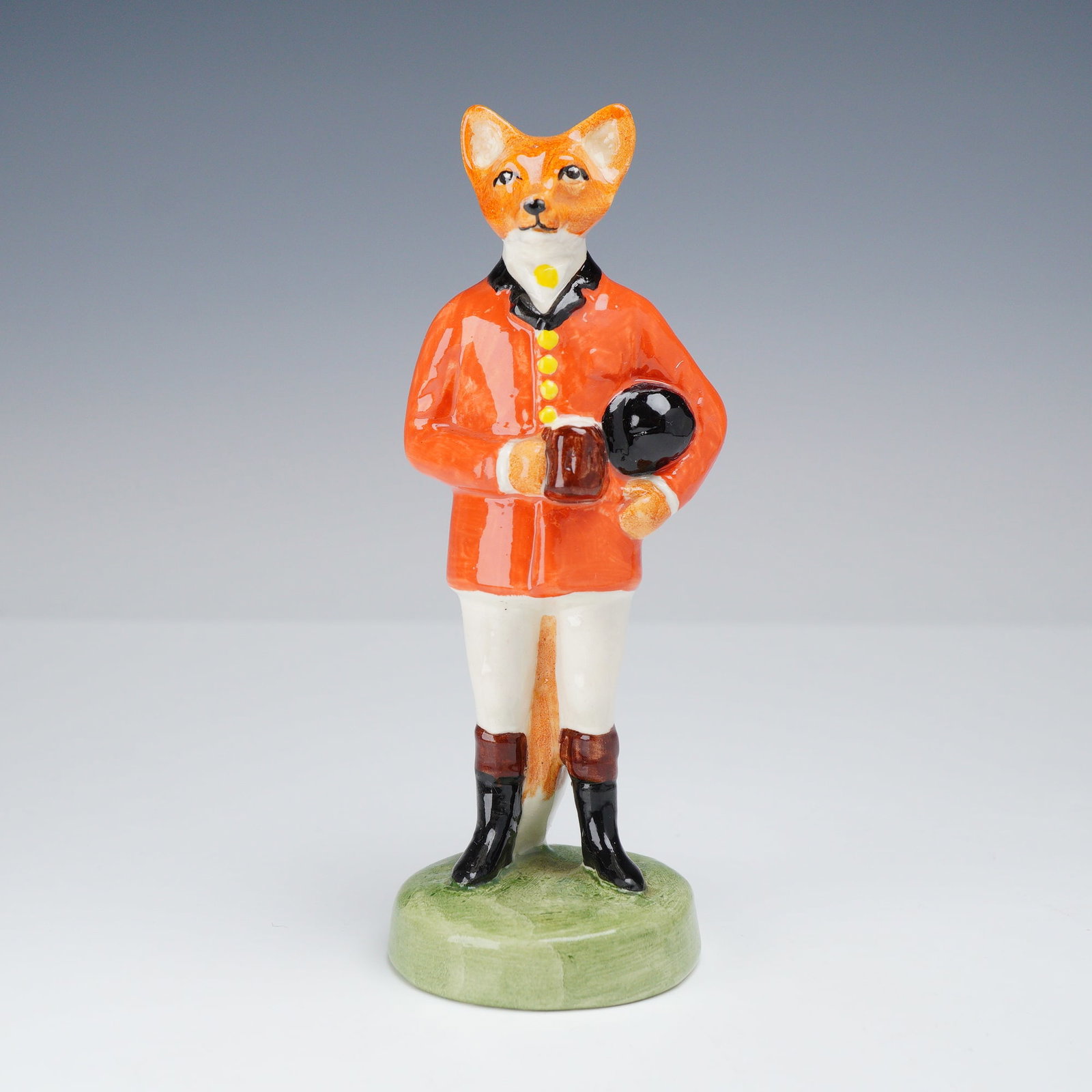 Gray's Pottery Staffordshire Figurine, Huntsman Fox Holding Mug: This glazed ceramic figurine by Gray's Pottery depicts an anthropomorphic huntsman fox in traditional English hunting attire. The figure is modeled standing on a circular green base, wearing a bright 