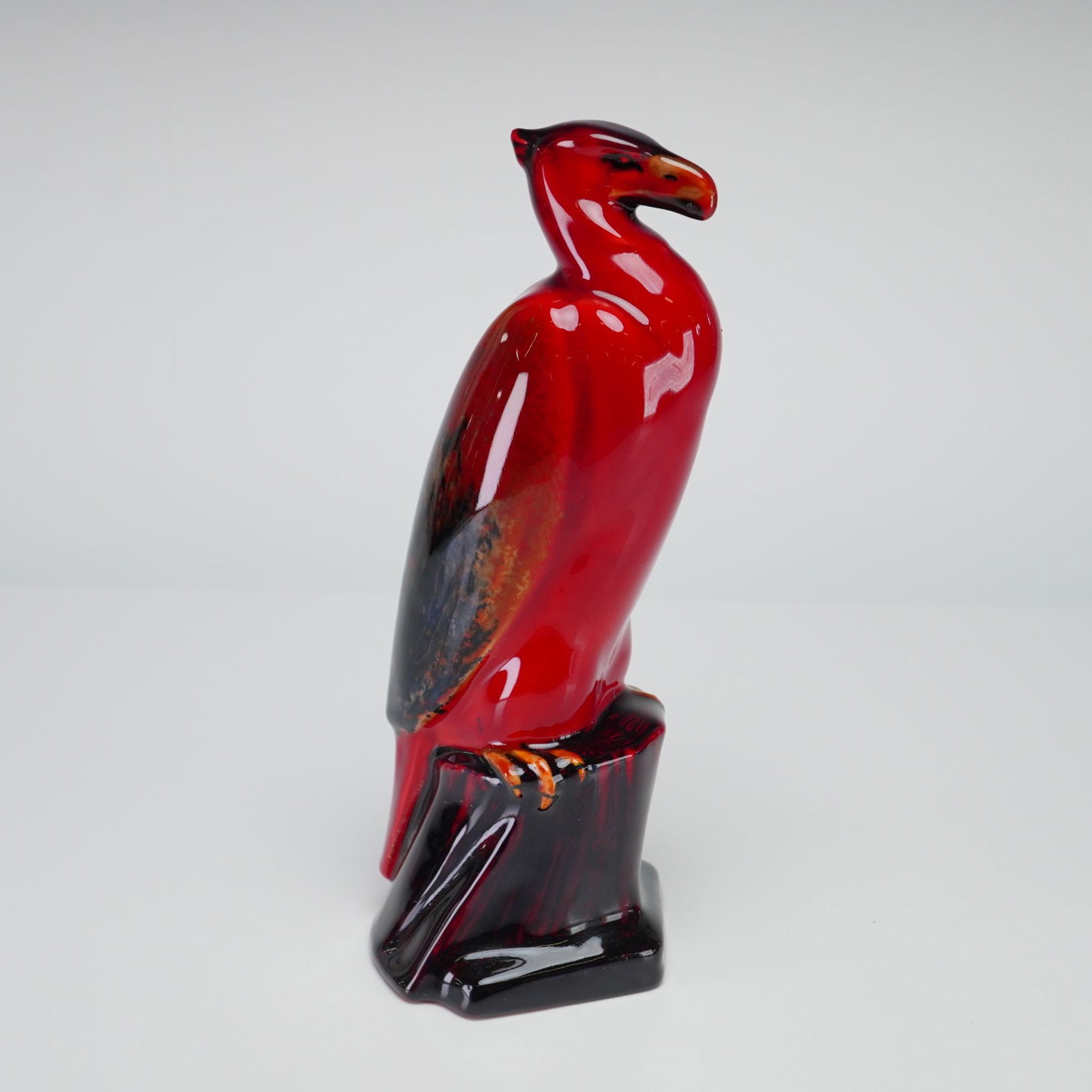 Royal Doulton Experimental Flambe Figurine, Eagle on Rock HN139: Figure depicting an eagle perched on a rocky outcrop. The ceramic piece is finished in a vibrant, high gloss flambe glaze featuring a deep red ground with mottled accents of dark purple, black, and bu