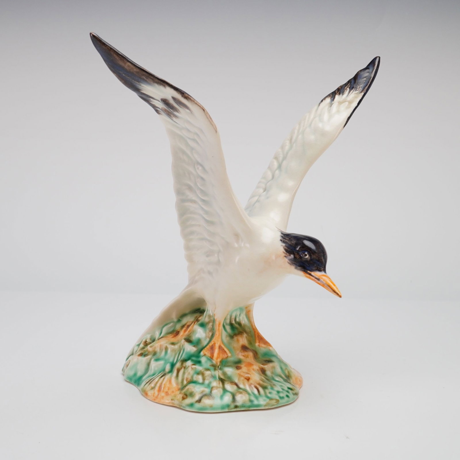 Rare Beswick Figurine, Seagull On Rock: Depicting a seagull with raised wings, positioned standing above a naturalistic rocky base. The bird features a white body with a black head and wingtips, and a hand-painted beak. The base is glazed i