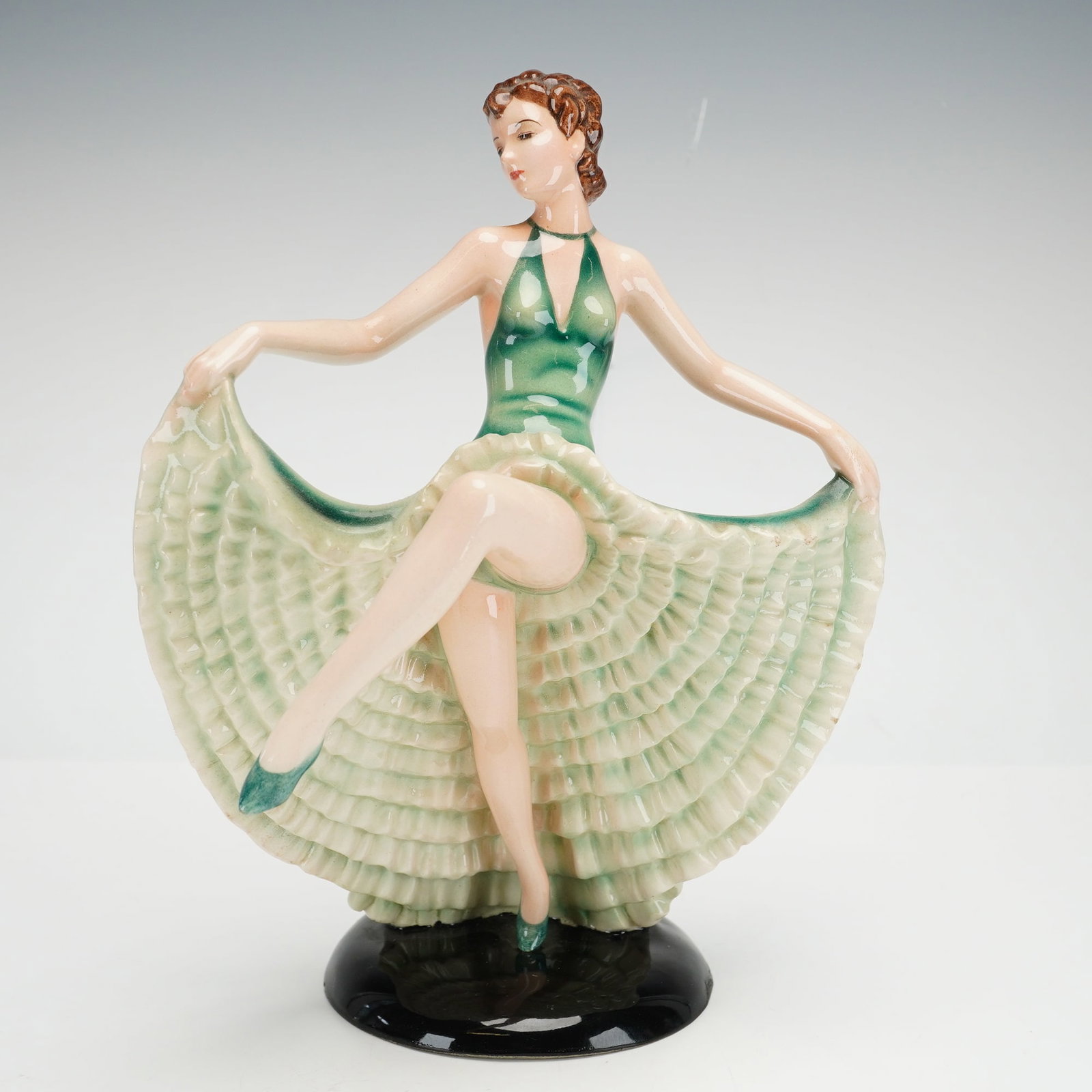 Keramos Wien Art Deco Glazed Ceramic Dancer Figurine: This Art Deco style glazed ceramic figurine depicts a female dancer in a dynamic pose. The figure is portrayed with her head turned and one leg raised, dressed in a green halter-top bodice and an expa