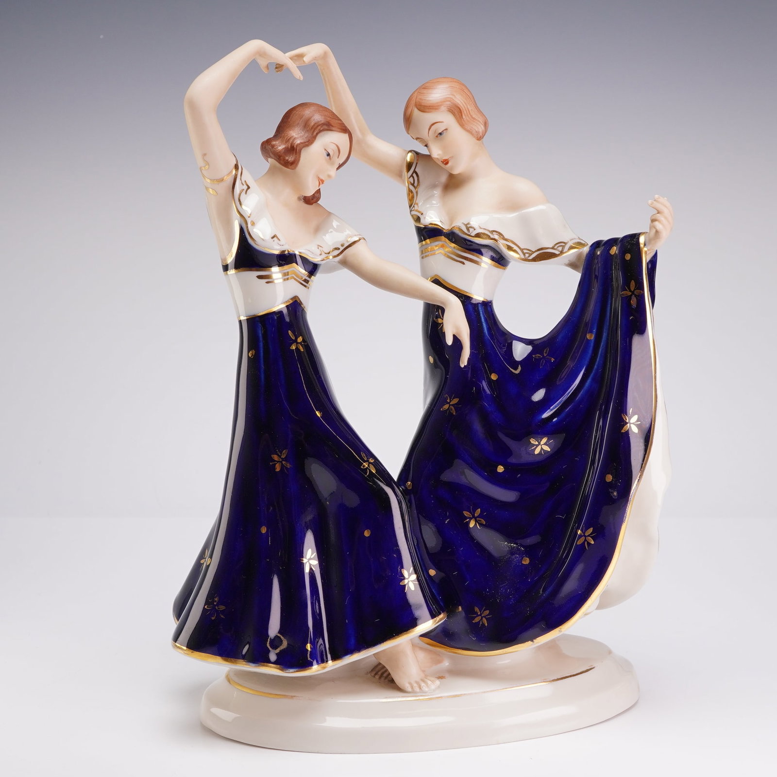 Elly Strobach Konig for Royal Dux Bohemia Art Deco Porcelain Figurine, Dancing Sisters: A Royal Dux Bohemia porcelain figurine designed by artist Elly Strobach and manufactured in Czechoslovakia. The piece depicts two young women in a synchronized dance pose on an oval white base. The fi