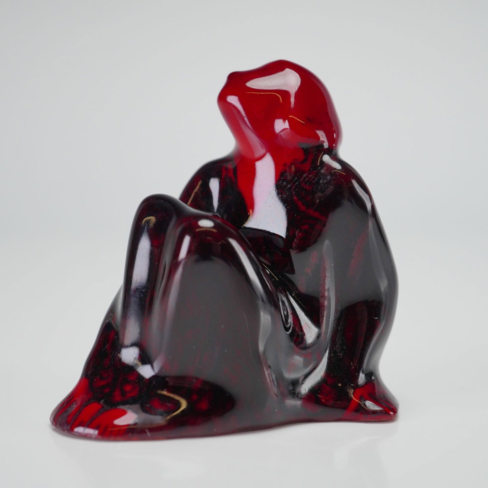 Royal Doulton Experimental Flambe Figurine, Grief HN595: Normally seen in blue, this figure of Grief is presented here in a rich red flambe glaze. The abstract, stylized figure is seated with knees drawn to the chest and head slightly raised. The glaze show