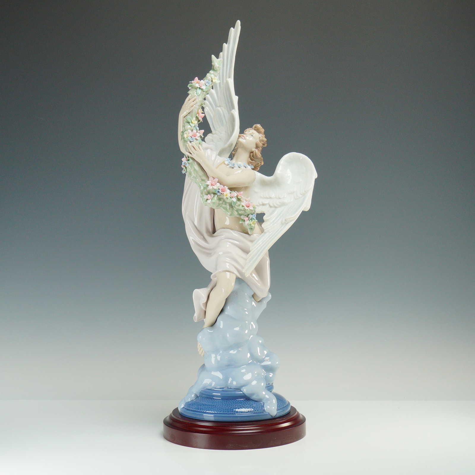 Lladro Limited Edition Porcelain Figurine Celestial Ascent 01001851, Signed: This limited-edition of 1500 piece depicts a winged celestial figure ascending from a base of stylized blue clouds. The figure is partially draped in a flowing, pale pink garment and holds an extensiv