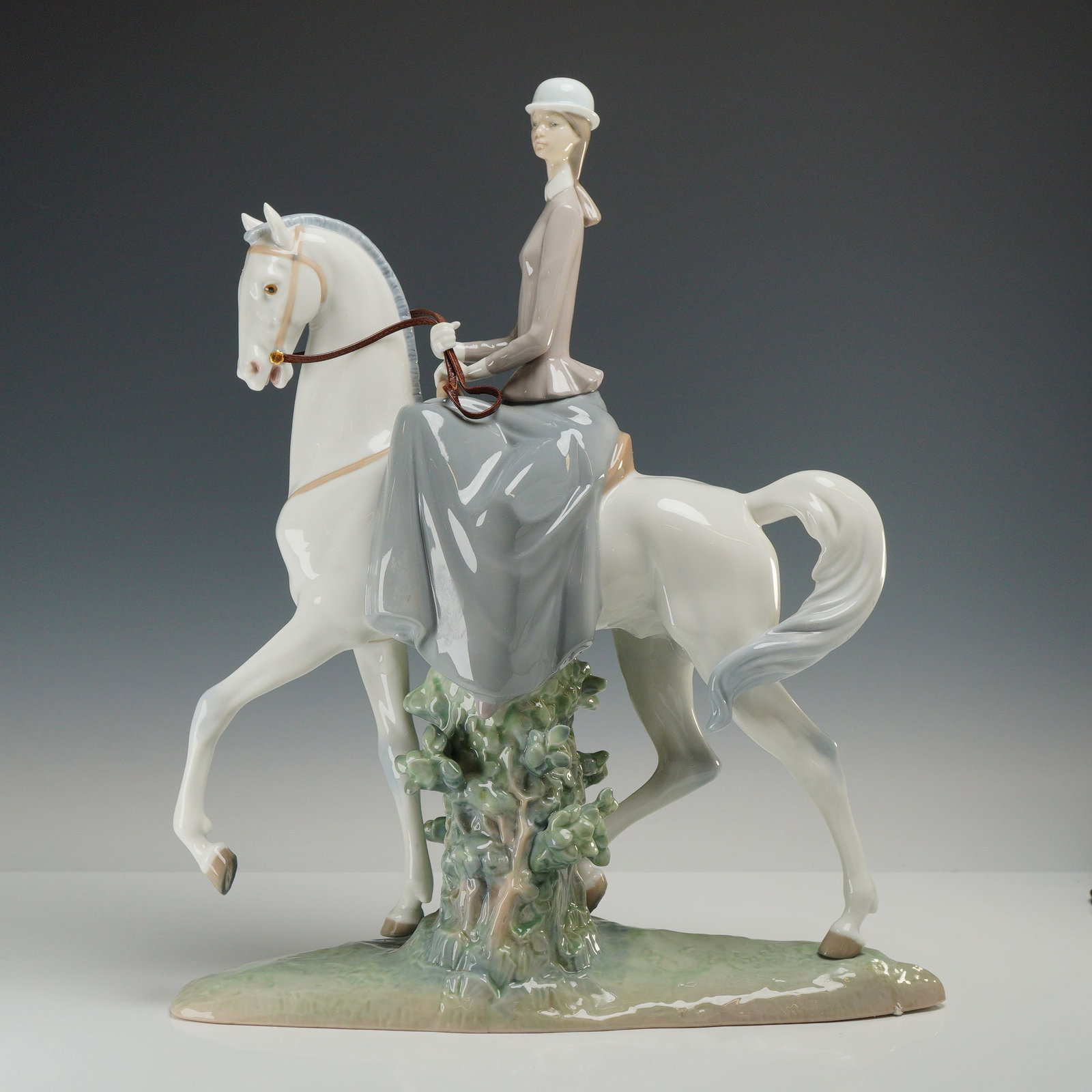 Lladro Porcelain Figurine, Female Equestrian 01004516: A large, glazed porcelain figurine manufactured by Lladro and designed by sculptor Fulgencio Garcia. The figurine depicts a woman in formal equestrian dress, consisting of a gray jacket, a white ridin