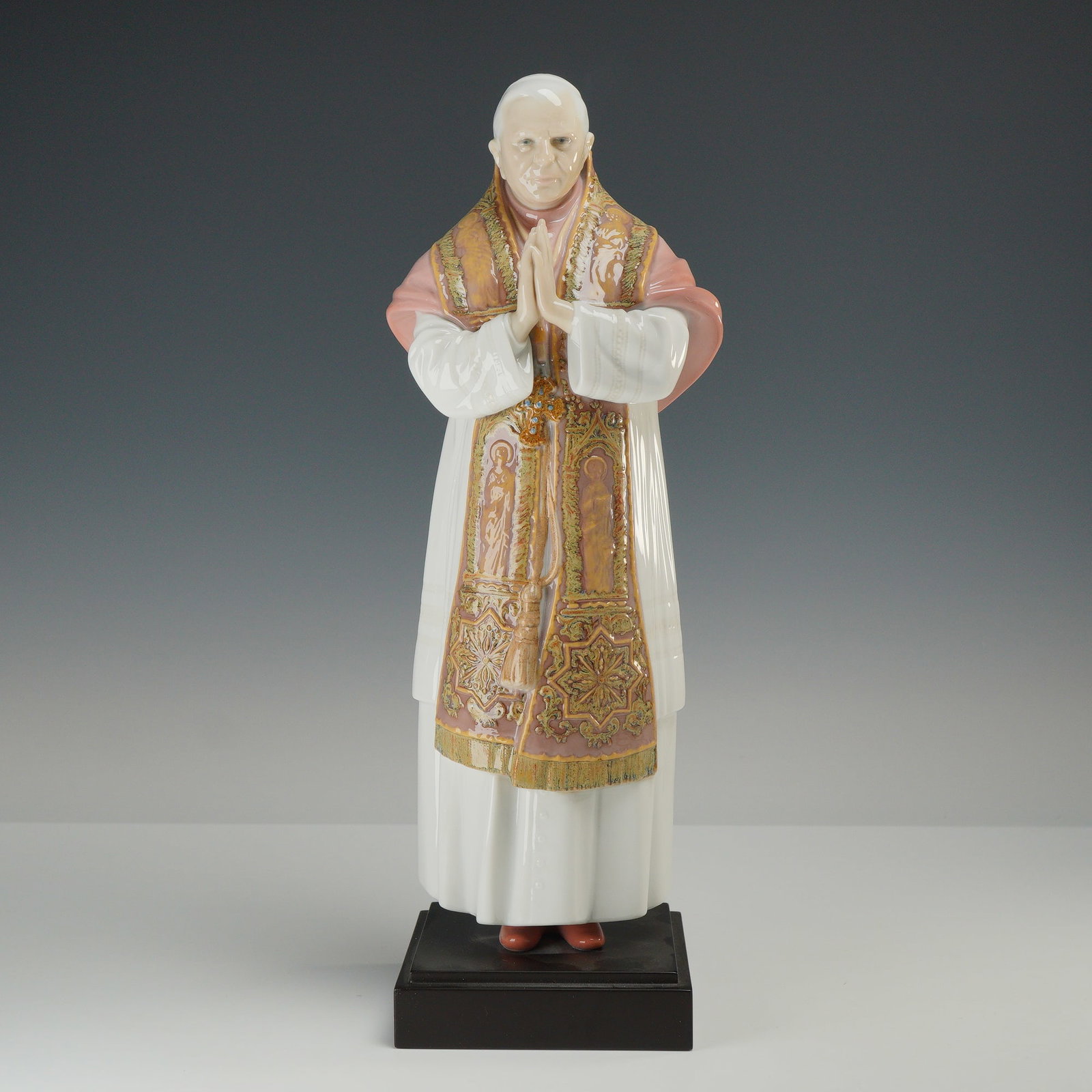 Lladro Porcelain Figurine Benedictus XVI 01008266: A Lladro polychrome glazed porcelain figurine designed by sculptor Juan Herrera. The figure depicts Pope Benedict XVI in a standing, prayerful pose with hands clasped. He is dressed in traditional pap