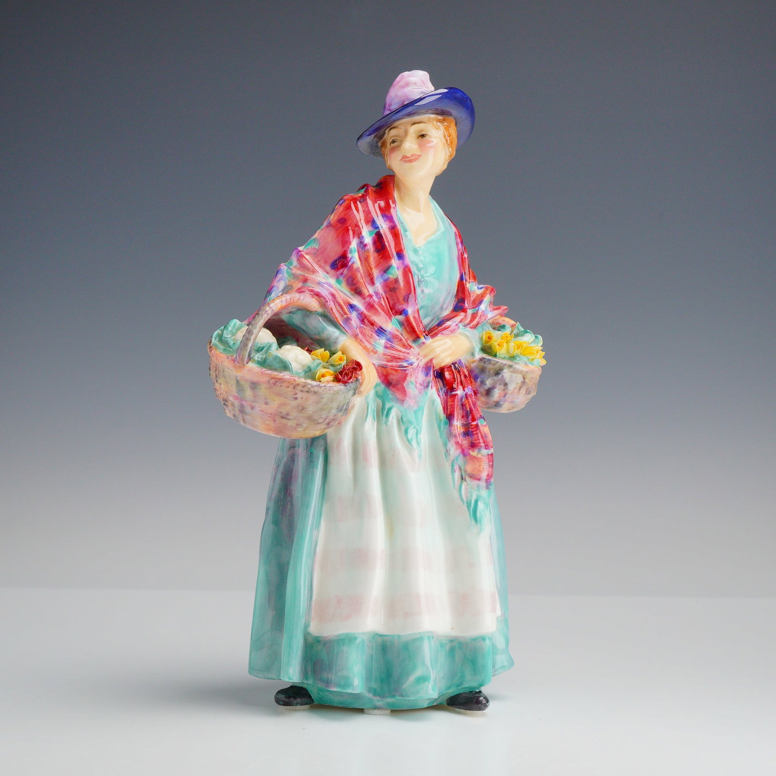 Royal Doulton Figurine Romany Sue HN 1757: This Royal Doulton bone china figurine, titled Romany Sue and designated as model HN 1757, depicts a standing woman in a teal gown and white apron. She is draped in a large, vibrantly colored shawl fe