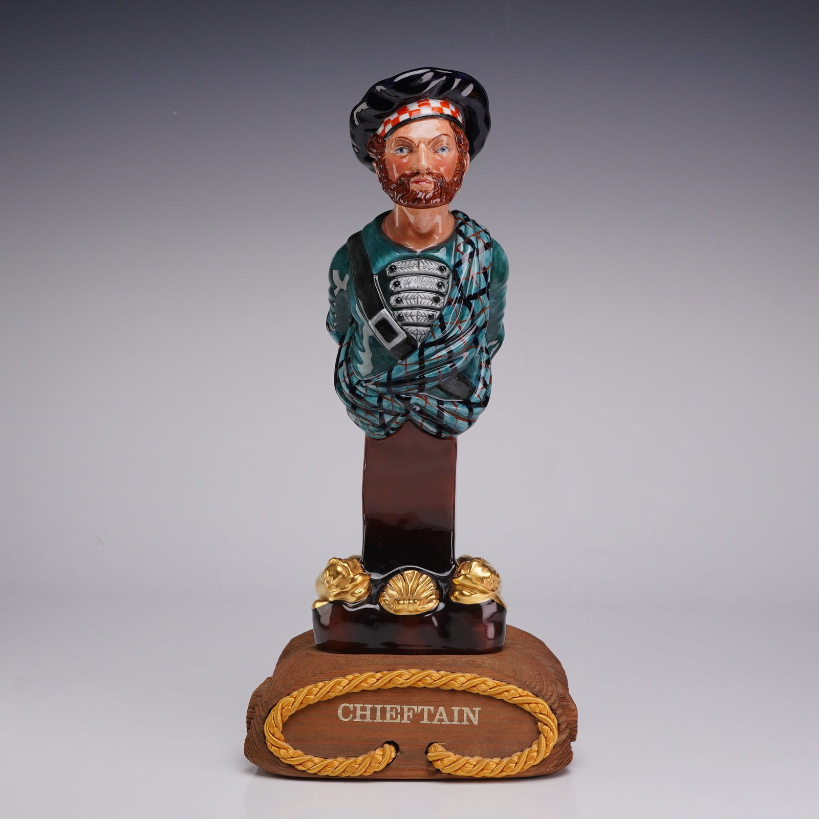 Royal Doulton Limited Edition Ships Figureheads, Chieftain HN2929: This piece is designed as a bust-style ship figurehead depicting a bearded Scottish man. He is wearing a black bonnet with a red and white checkered band and a red pom-pom on the back. The attire incl