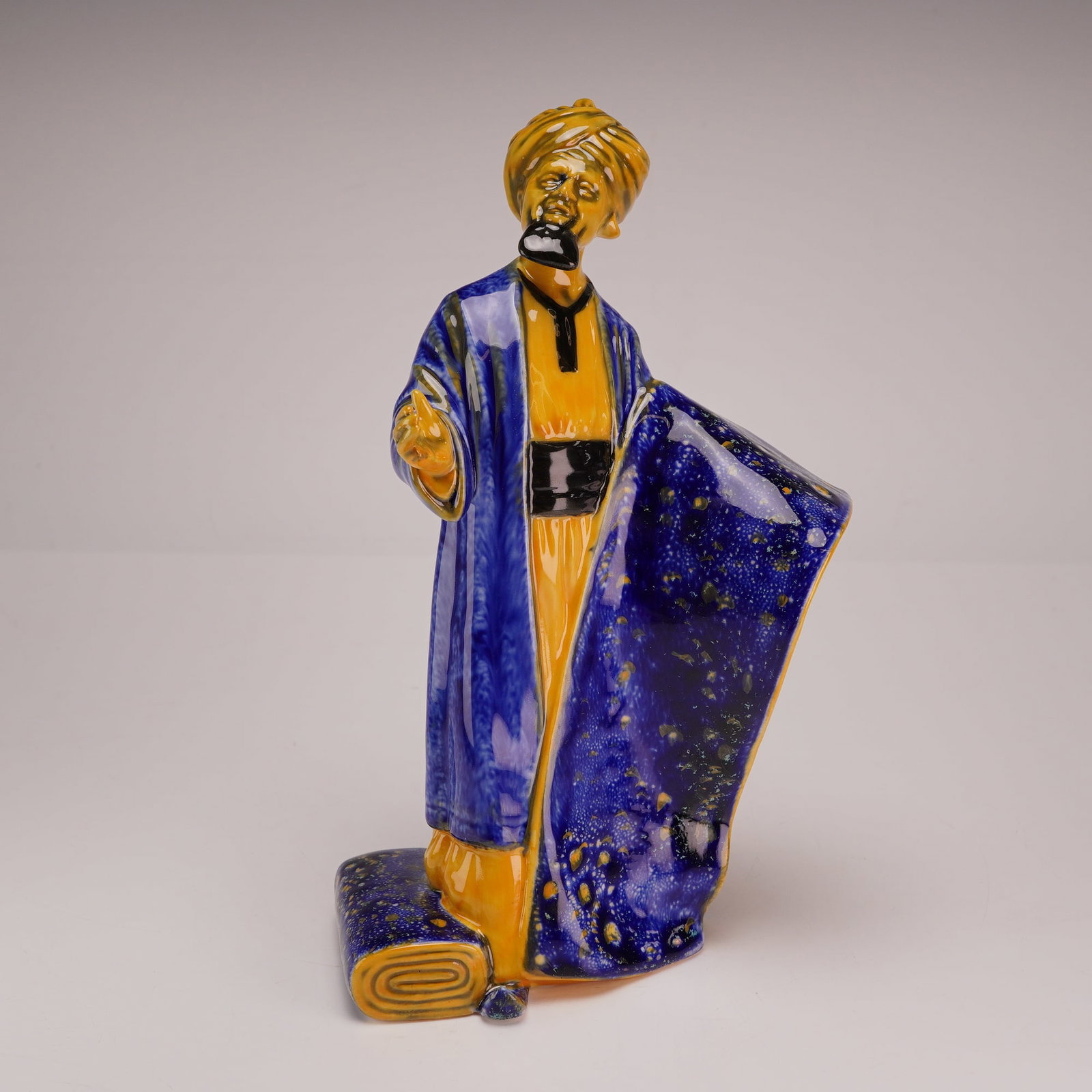Royal Doulton Flambe Porcelain Figurine The Carpet Seller HN 2776: This Royal Doulton porcelain figurine is titled The Carpet Seller, model number HN 2776, from the Flambe collection. The piece was modeled by William K. Harper and is dated 1990. The figurine depicts 