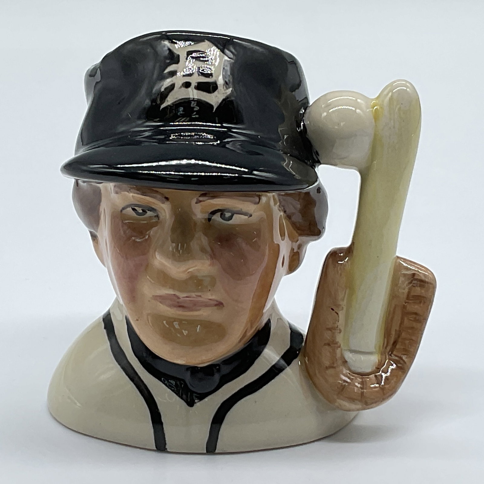 Royal Doulton Prototype Mini Character Jug, Baseball Player: Hand painted miniature figural jug of a baseball player for the Detroit Tigers. White jersey with black highlights. A baseball glove, bat and ball forms the handle. Royal Doulton backstamp. Marked: Th