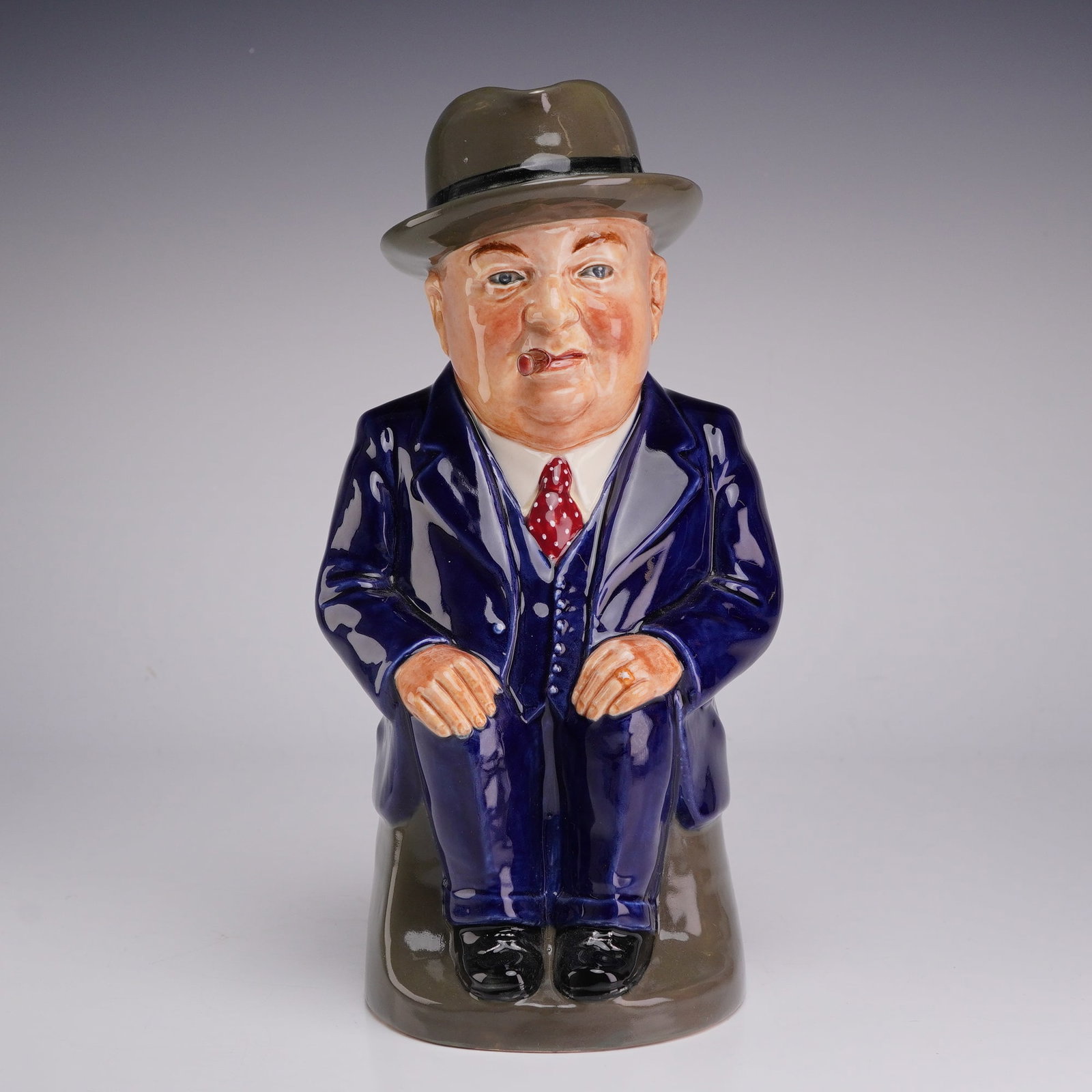 Royal Doulton Winston Churchill Toby Jug, Greetings Cliff Cornell: A Royal Doulton glazed ceramic Toby jug depicting Sir Winston Churchill, produced as a promotional item for the Cleveland Flux Company. The figure is modeled in a seated pose, dressed in a navy blue t