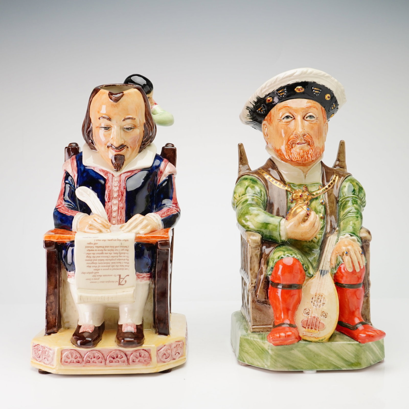 Two Kevin Francis Ceramics Limited Edition Toby Jugs, William Shakespeare and King Henry VIII: The first figure depicts William Shakespeare seated in a high-backed chair, wearing a dark blue doublet with red and white trim, white breeches, and brown shoes. He holds a quill pen in his right hand