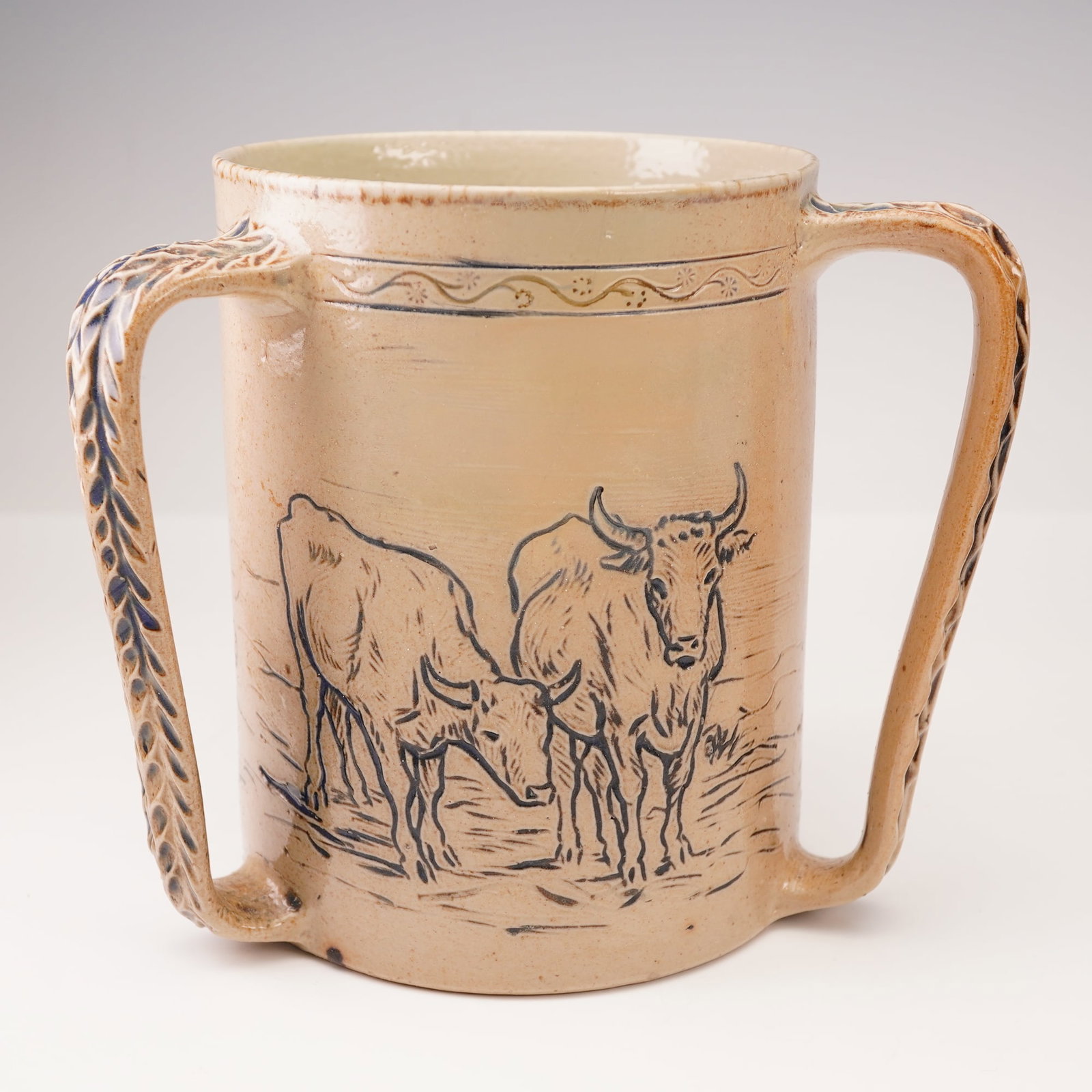 Doulton Lambeth Cattle Motif Tyg by Hannah Barlow: This Doulton Lambeth tyg features a detailed incised cattle motif, masterfully executed by renowned artist Hannah Barlow. The design showcases intricately carved images of cattle, demonstrating Barlow