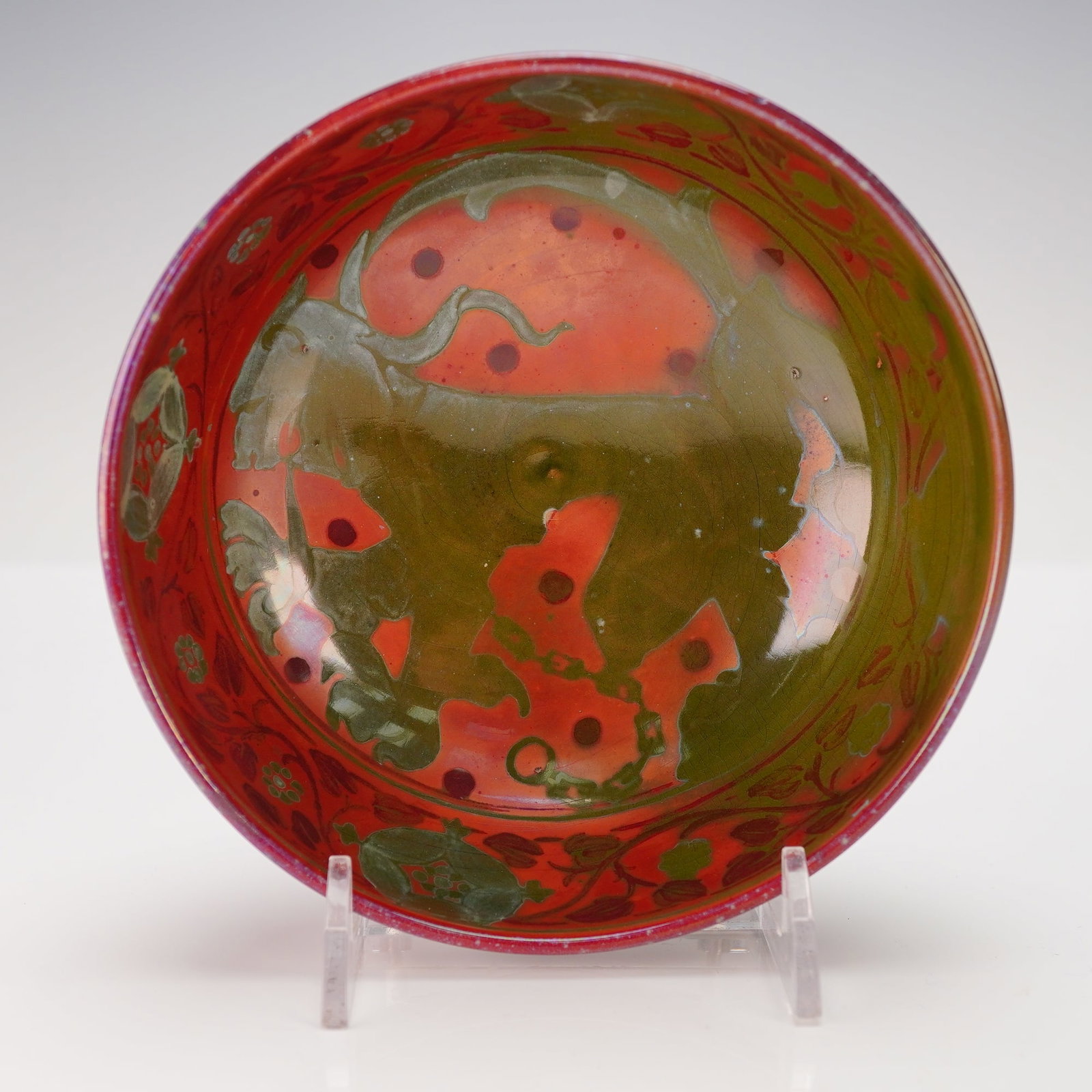 Bernard Moore Flambe Mystical Lion Lustreware Bowl: A rounded form bowl enveloped in a richly iridescent glaze with tones of crimson, olive, and rose. The exterior of the bowl is decorated with stylized floral and foliate motifs and the interior is des