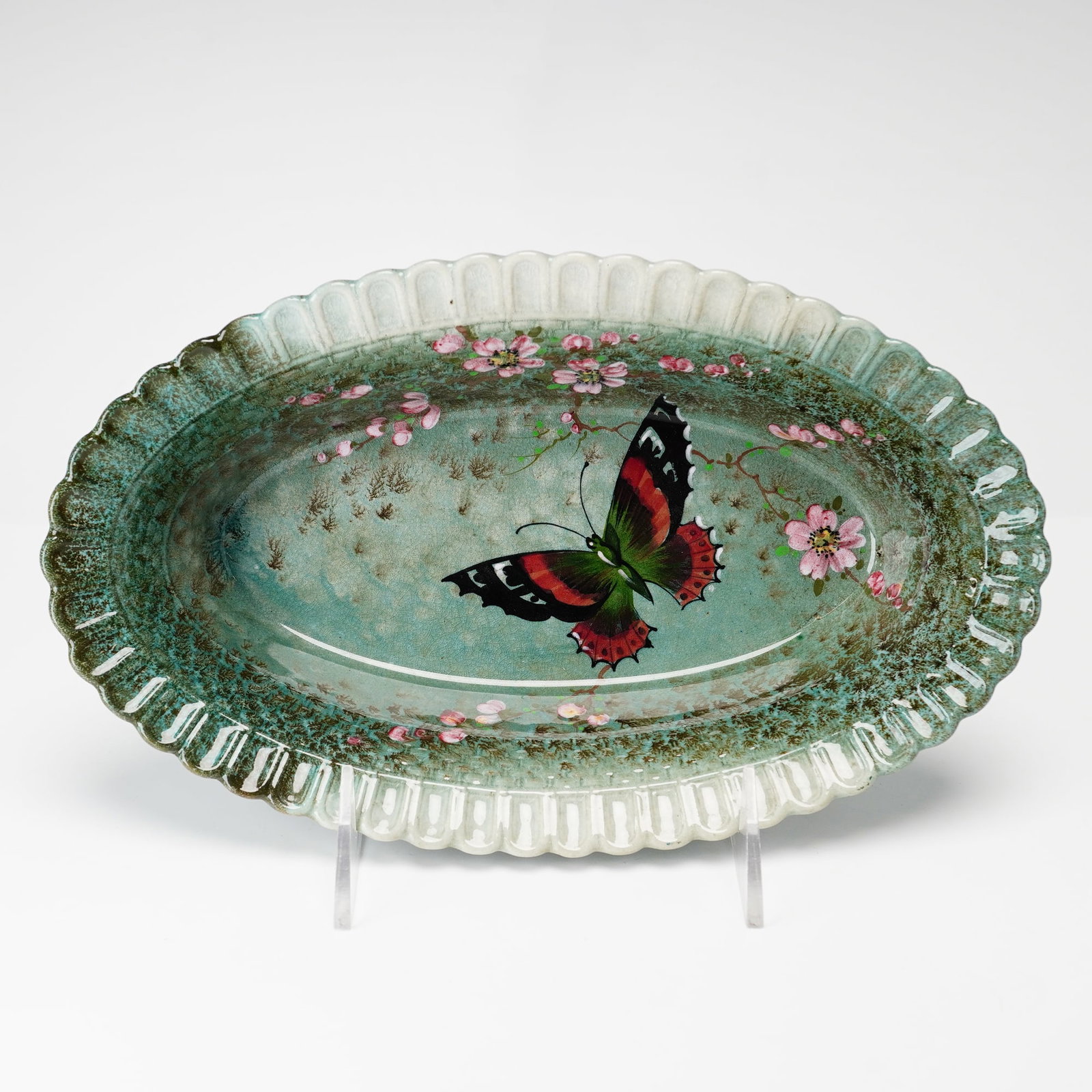 Royal Doulton Titanian Ware Oval Fluted Butterfly Bowl: This Royal Doulton Titania ware bowl is an oval form featuring a deeply fluted and scalloped rim. The ceramic is finished in a mottled teal-green crystalline glaze. The interior is decorated with a ha
