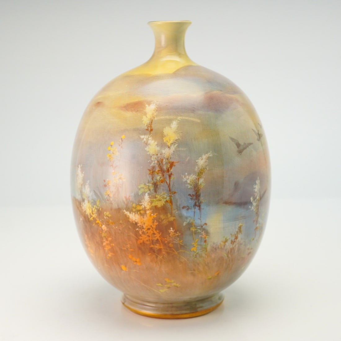 Doulton by Joseph Hancock Lakeside Scene Vase: Scene painted vase on ovoid form, decorated in the round with an extensive mountain lake view of flying geese and herons. Colored in soft pastels. Gilt accents in neck and base. Joseph Hancock signed 