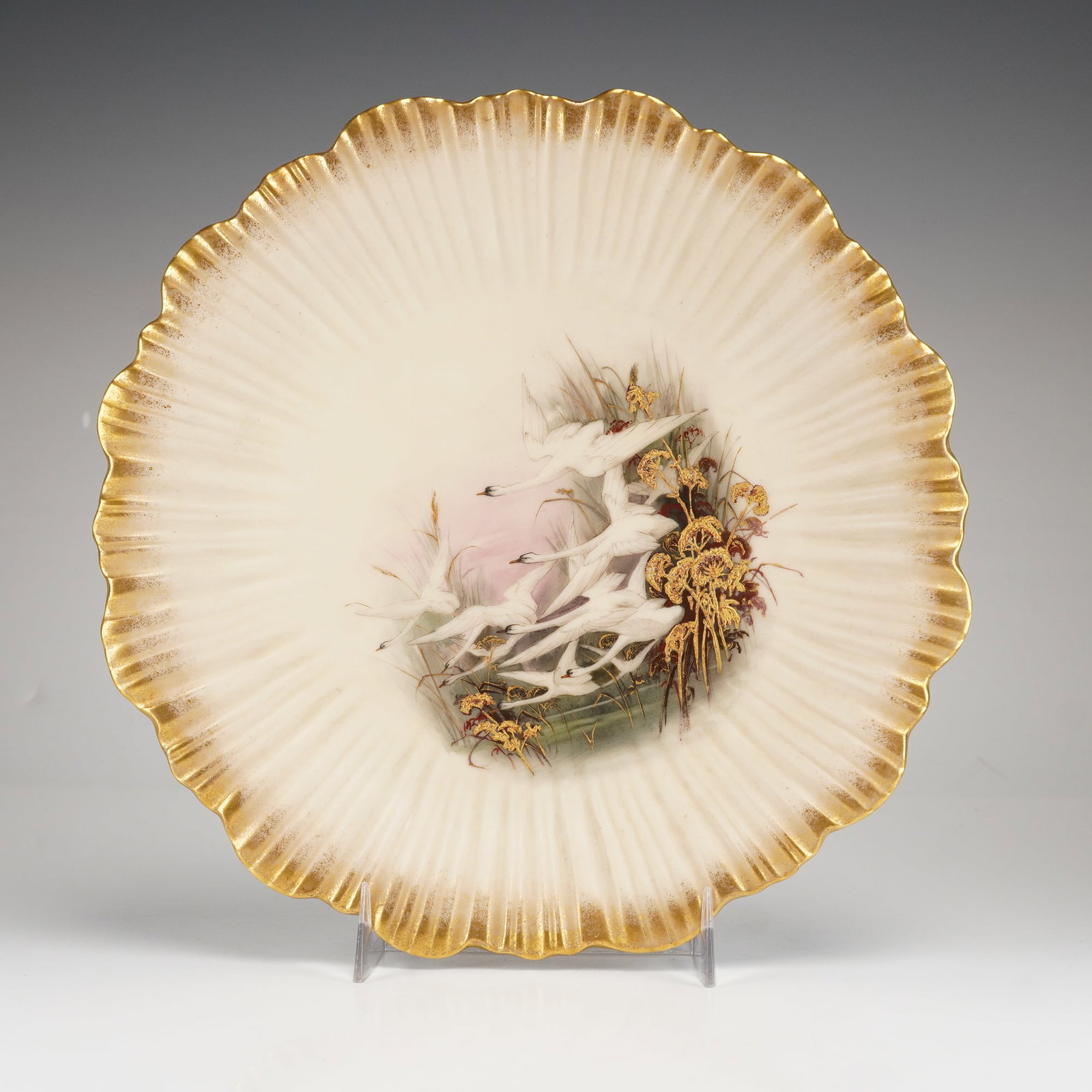 Royal Worcester Painted Porcelain Swan Cabinet Plate: A Royal Worcester porcelain cabinet plate of circular form featuring a heavily fluted and scalloped rim. The central well is hand-painted with a scene depicting six white swans in flight over a marshl