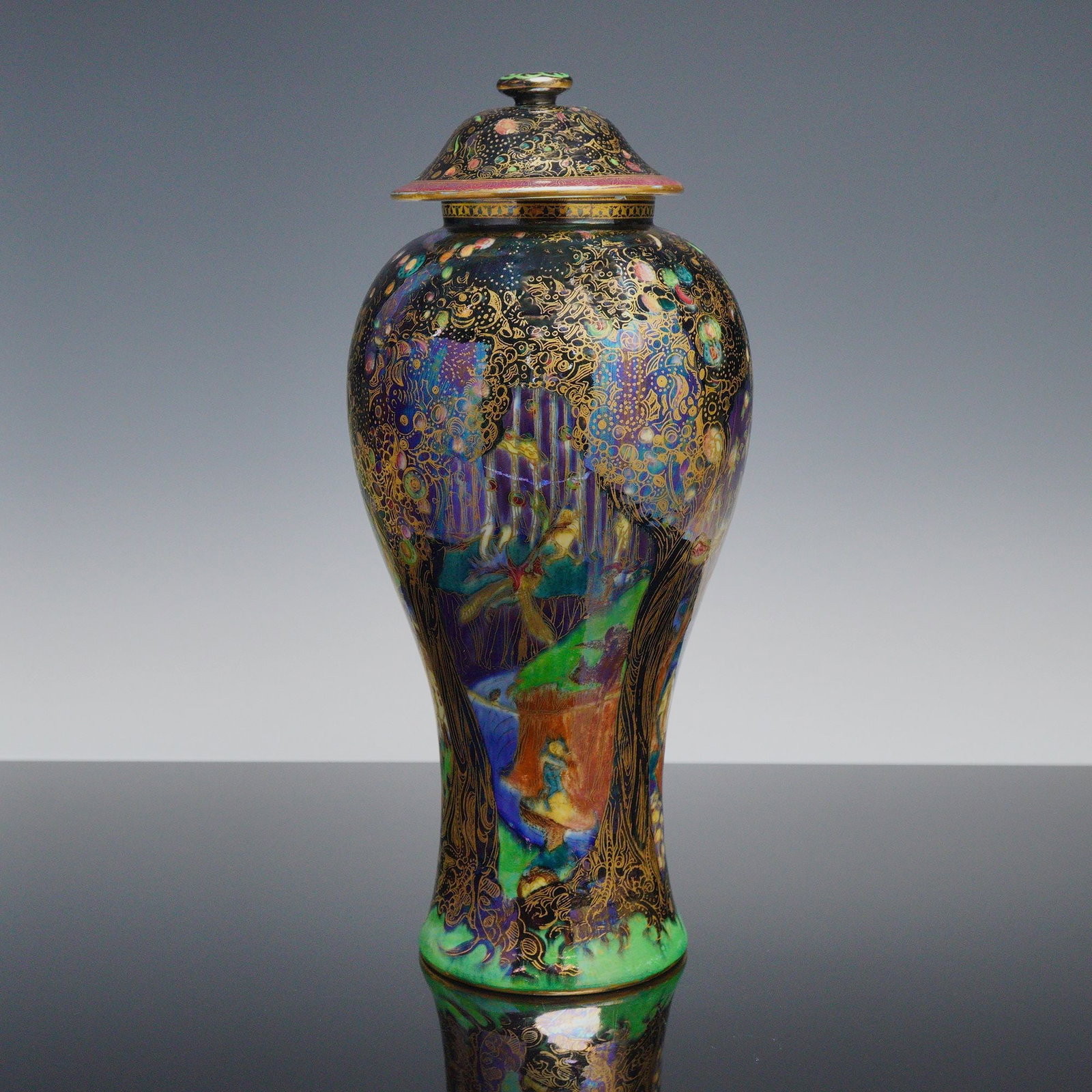 Wedgwood Fairyland Lustre Lidded Vase, Jewelled Tree with Cat and Mouse and Copper Trees Z4968: Designed by Daisy Makeig-Jones. The scene shows a black tree with gilt and colored detailing set before a grassy rocky formation and a winding blue river with a bridge. A mouse and black cat appear at