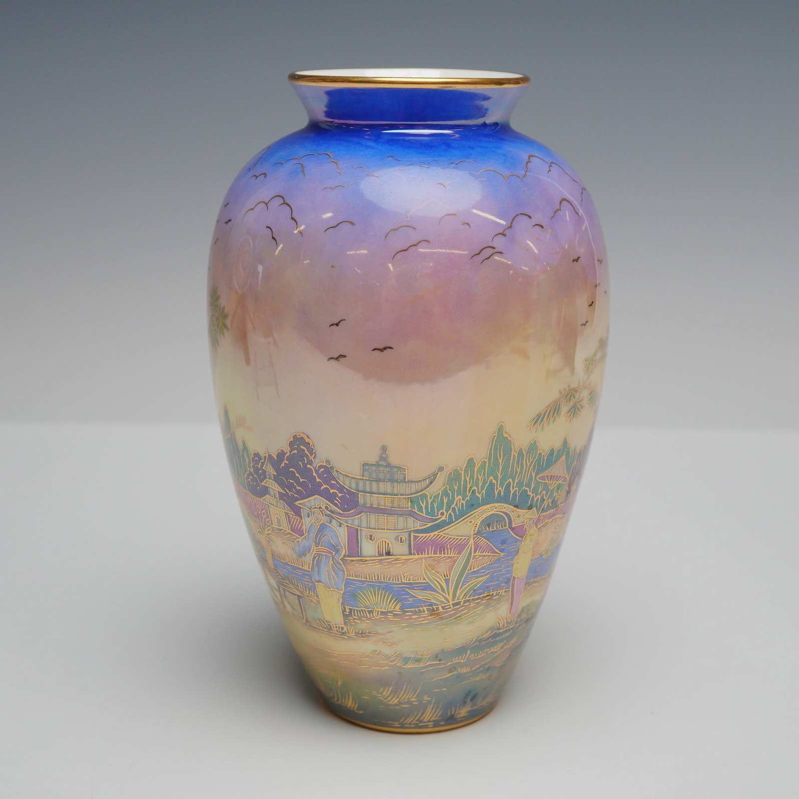 Wedgwood Fairyland Lustre Vase, Willow: This Wedgwood bone china vase features a tapered ovoid form with a short neck and a gilded rim. The exterior is decorated in a variation of the Chinoiserie Willow pattern, depicting an intricate lands