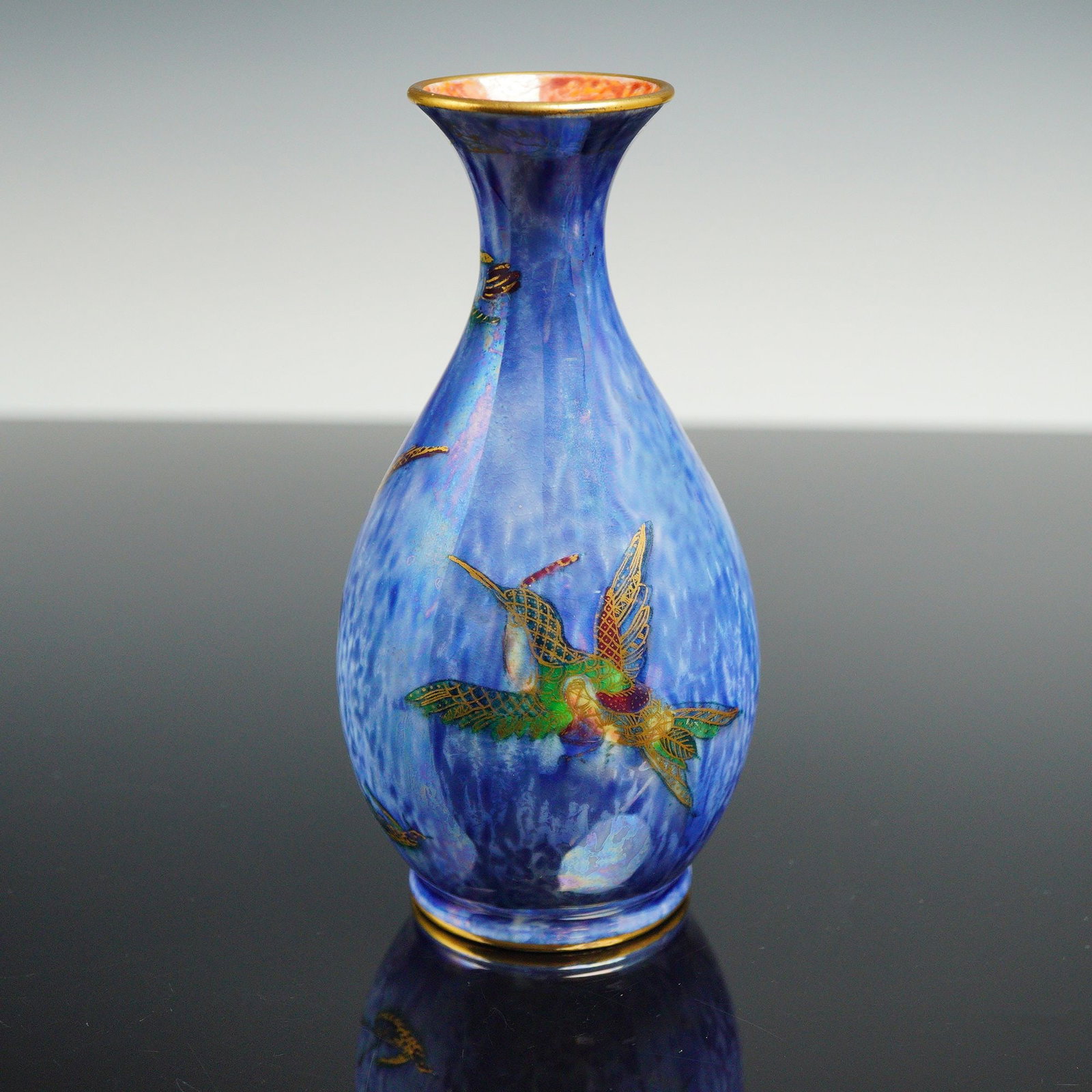 Wedgwood Fairyland Lustre Vase, Flying Humming Bird Z5294: Designed by Daisy Makeig-Jones. Small vase featuring a mixed blue exterior luster glaze, accented with gilt hummingbirds in green, red, and blue. The Flying Geese border decorates the top and bottom r